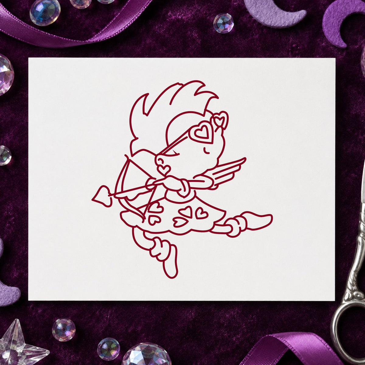 Cupid with Heart Sunglasses Rubber Stamp impression in burgundy ink on white paper in a styled craft setting.
