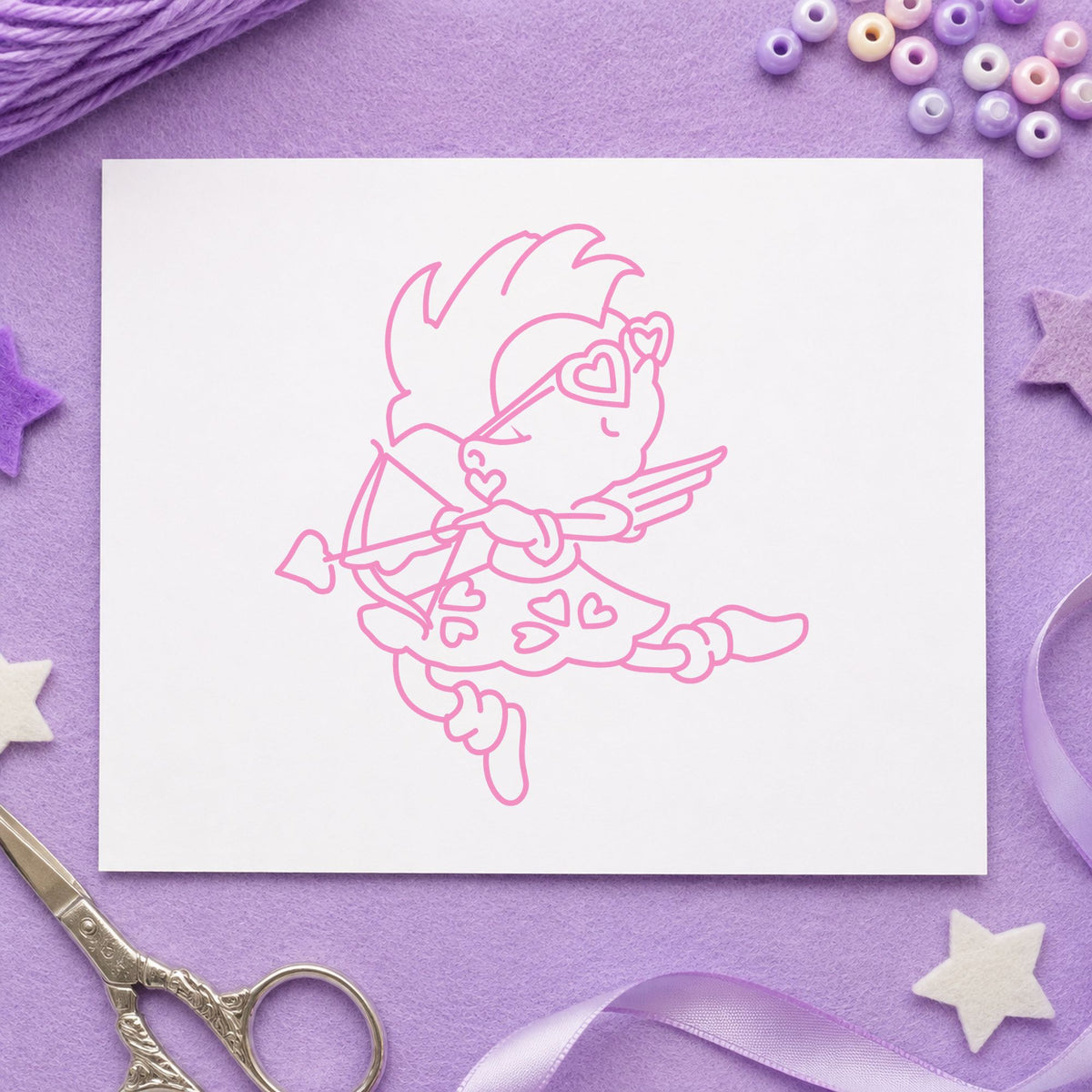 Cupid with Heart Sunglasses Rubber Stamp impression in pink ink on white paper in a styled craft setting.