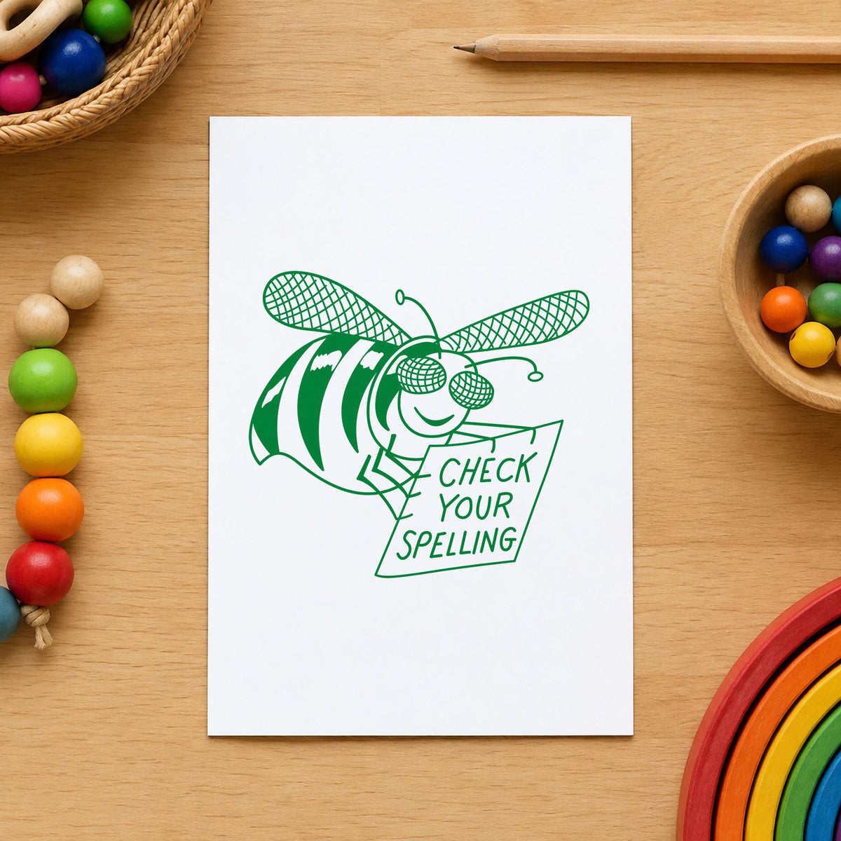 Check Your Spelling Bee Rubber Stamp impression in green ink on white paper in a styled craft setting.