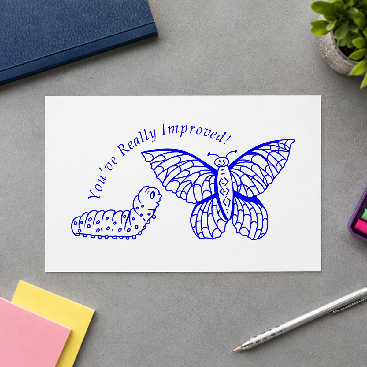 Youve Really Improved Butterfly and Caterpillar Rubber Stamp impression in blue ink on white paper in a styled craft setting.