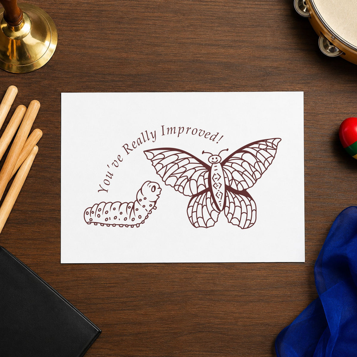 Youve Really Improved Butterfly and Caterpillar Rubber Stamp impression in brown ink on white paper in a styled craft setting.