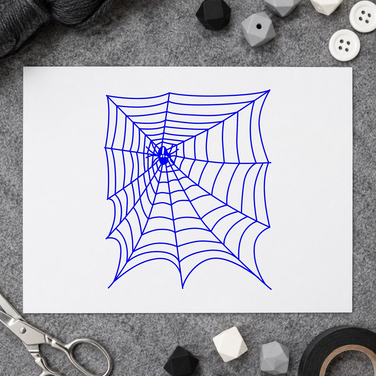 Spider and Web Halloween Rubber Stamp impression in blue ink on white paper in a styled craft setting.