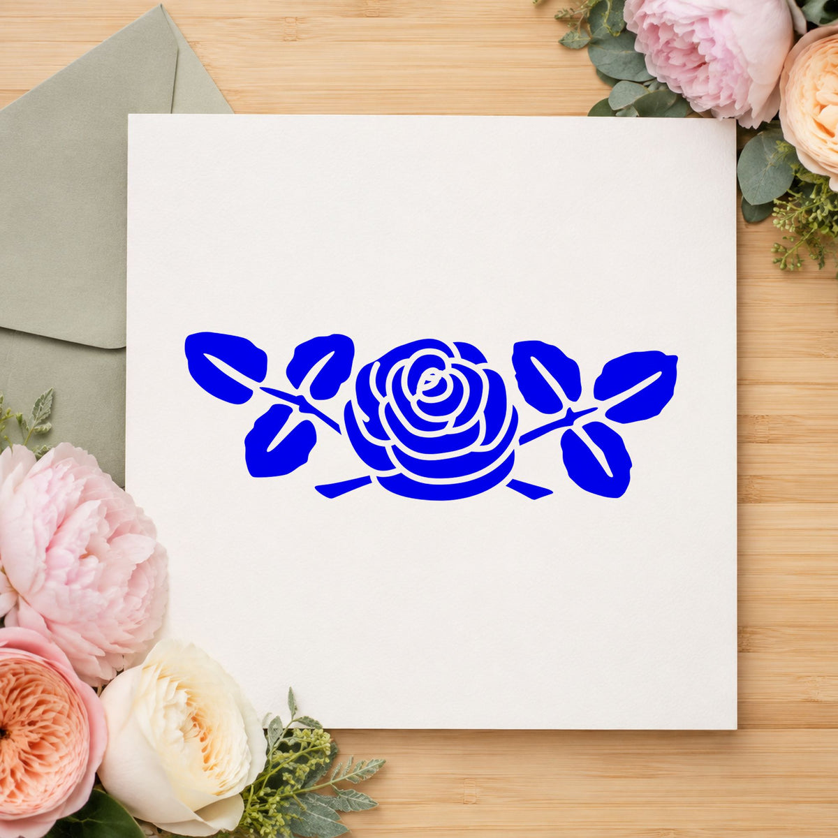 Rose with Leaves Rubber Stamp Small impression in blue ink on white paper in a styled craft setting.