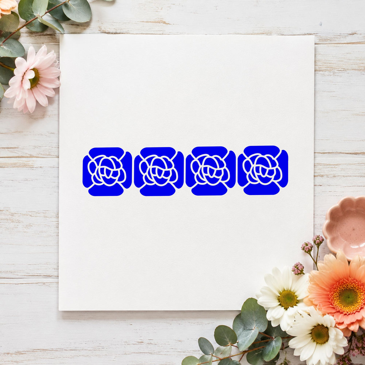 Blue scrapbook border stamp impression featuring the four solid flowers border design on white paper.