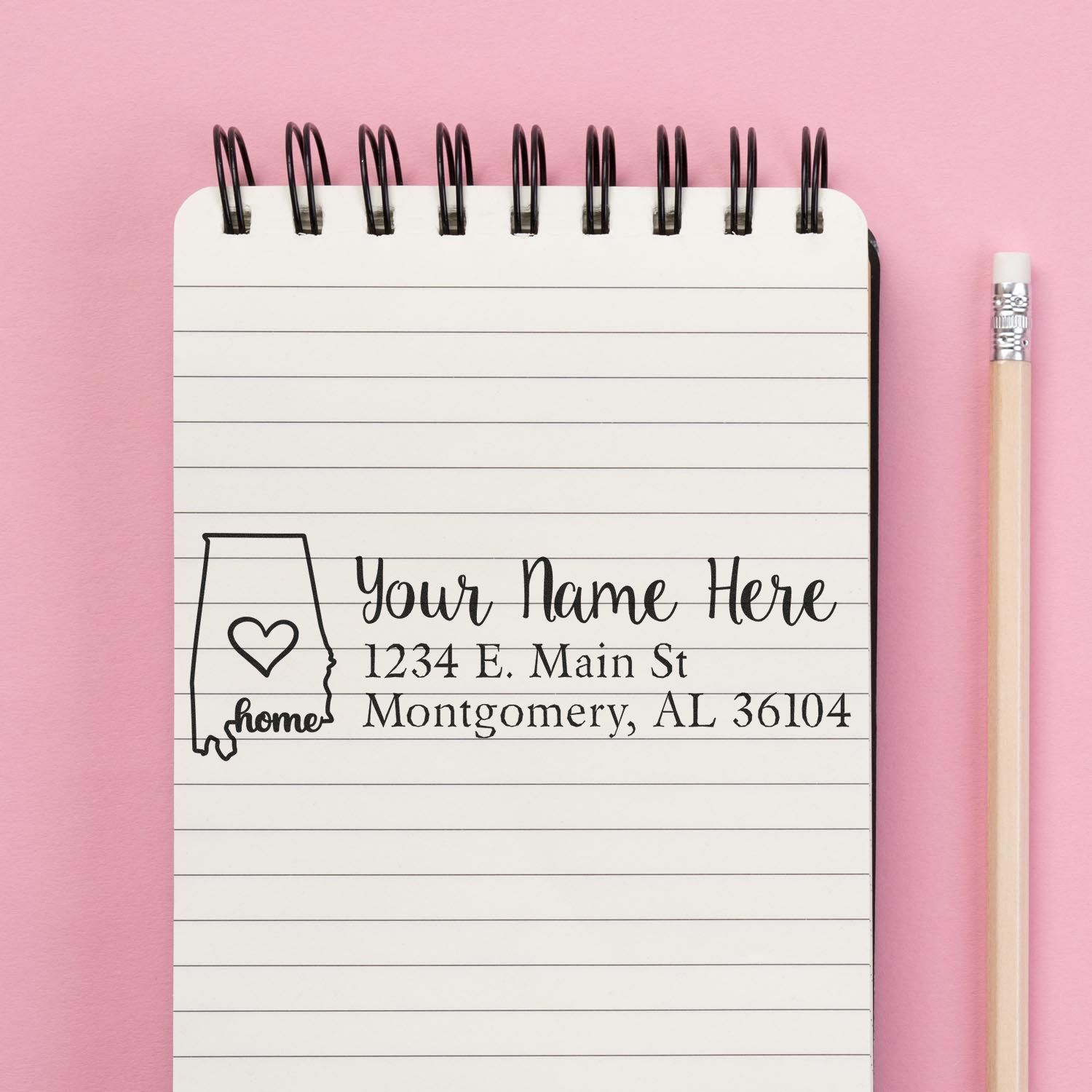 Personalized rubber return address stamp with Alabama home icon, name, and address on a notebook.