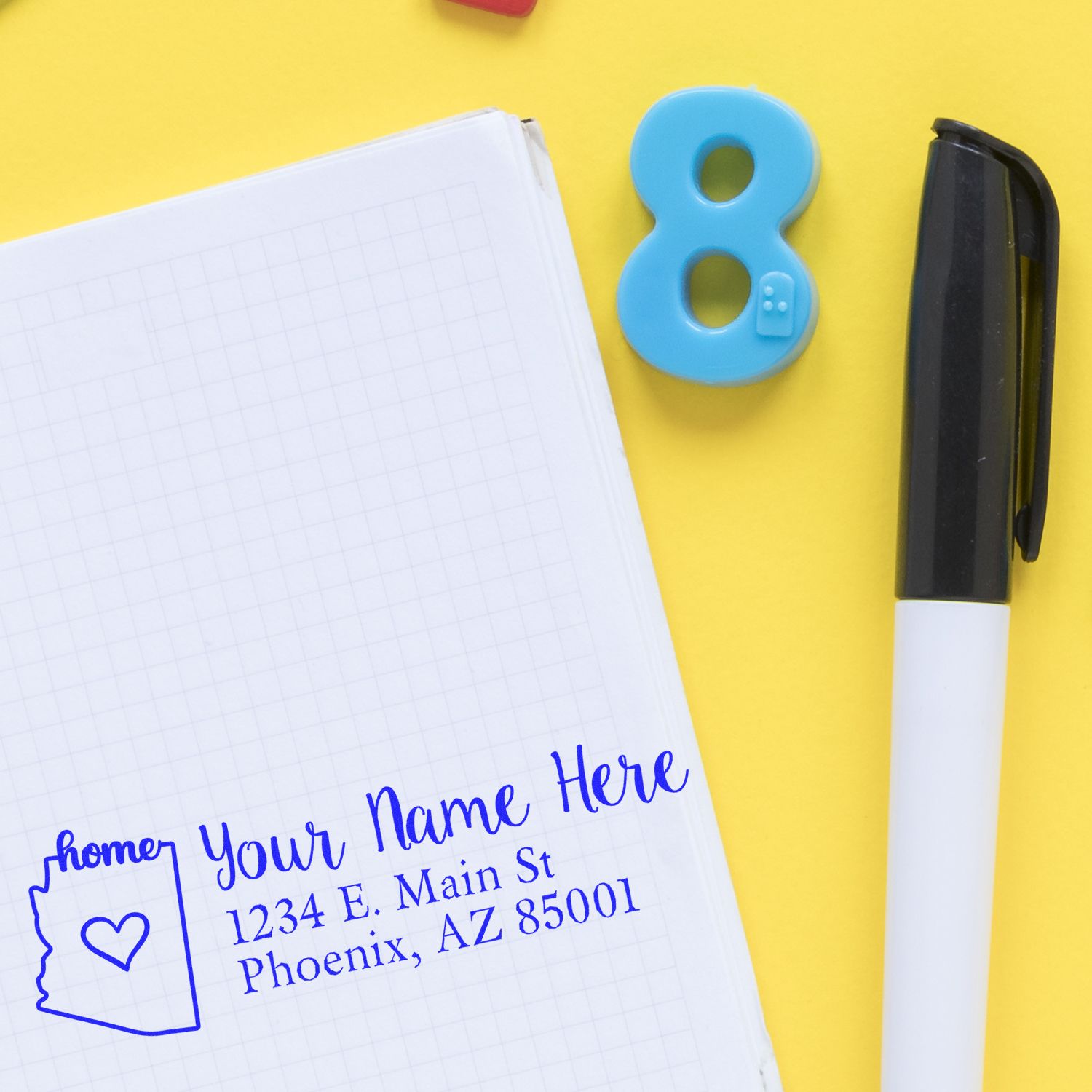Custom return address rubber stamp with house icon imprint on notebook beside marker and number 8, perfect for mailing and stationery.