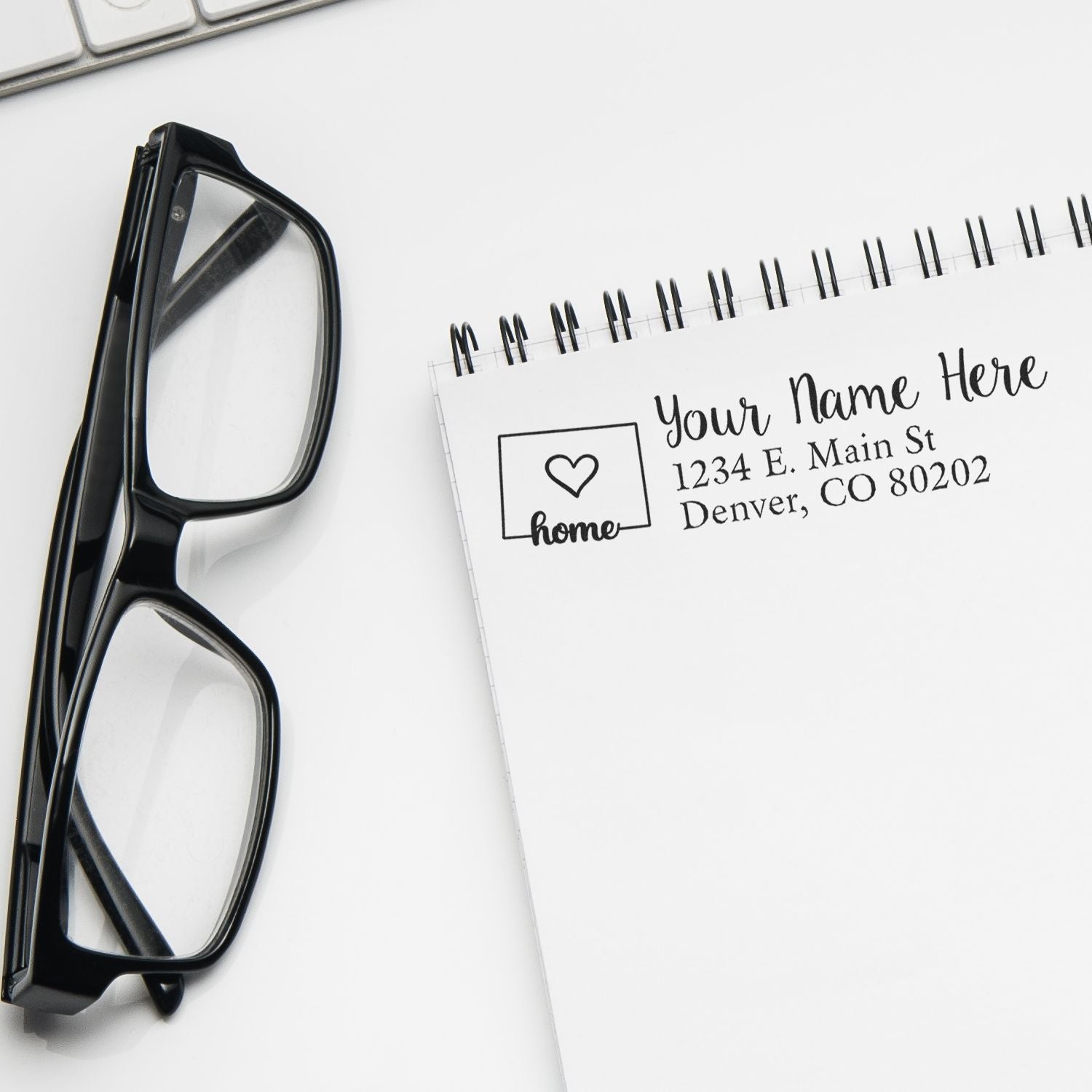 Personalized address rubber stamp with home icon and return address imprint on notebook beside eyeglasses