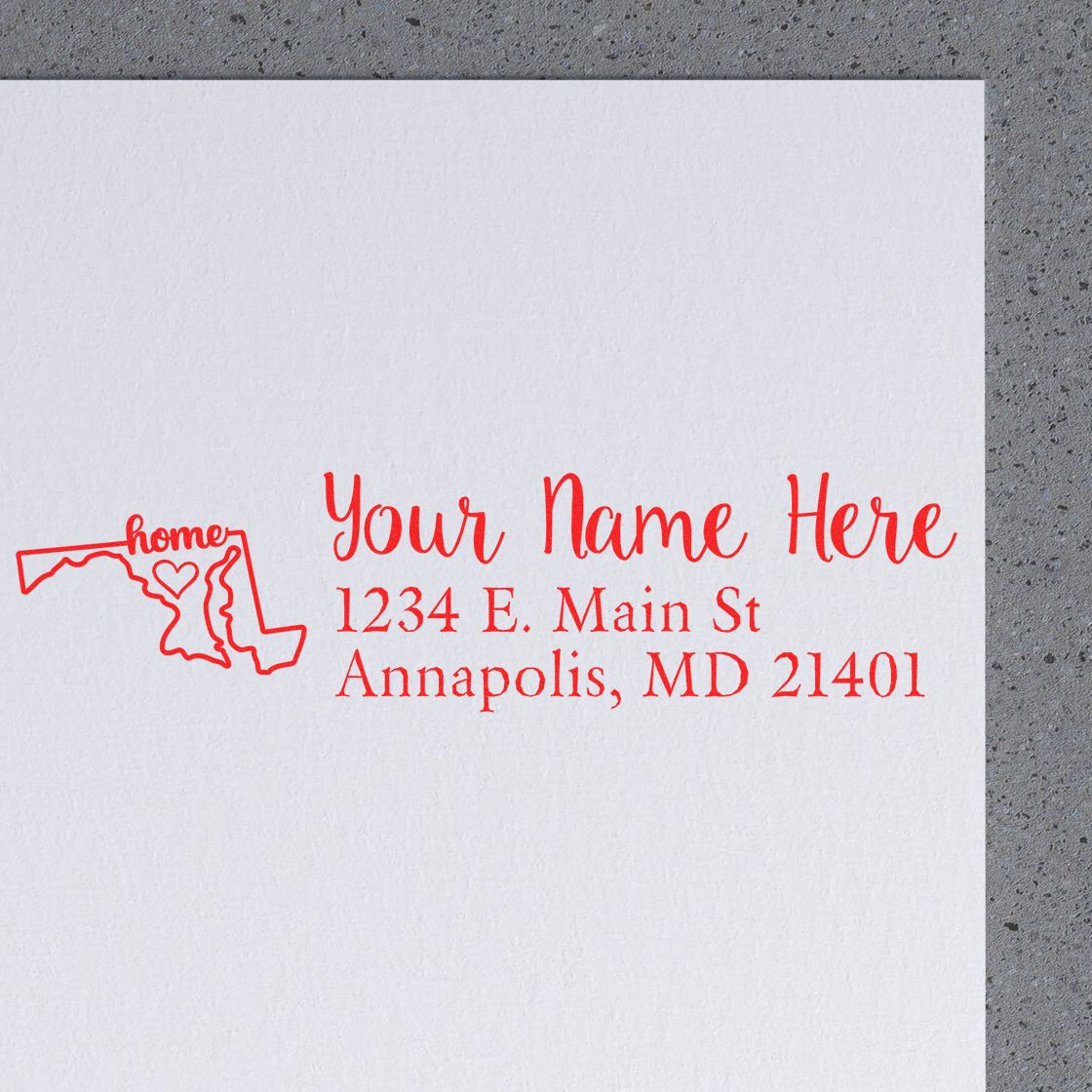 Personalized return address rubber stamp with Maryland home icon and Annapolis, MD address in red ink on white paper.