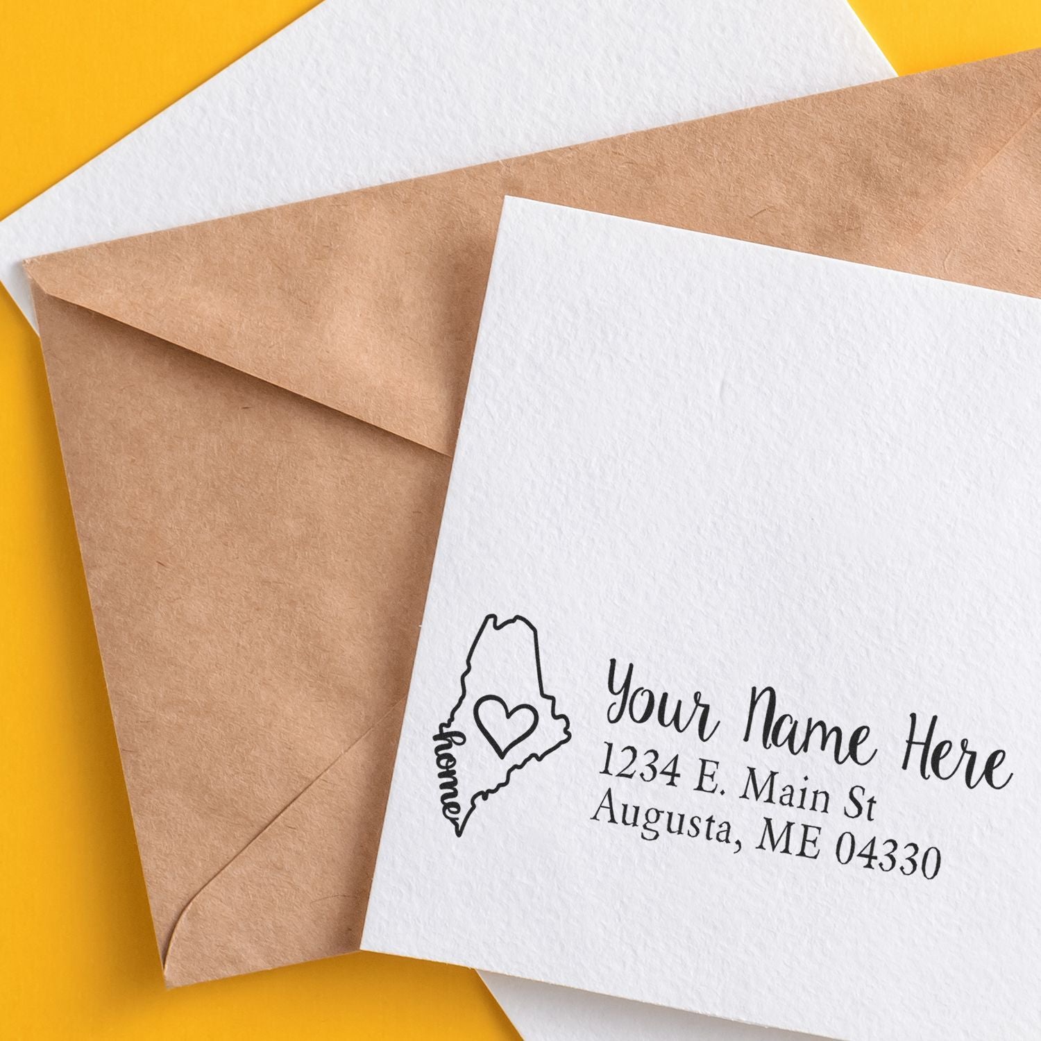 Custom return address rubber stamp on white envelope with Maine heart design, paired with a kraft envelope on yellow background.