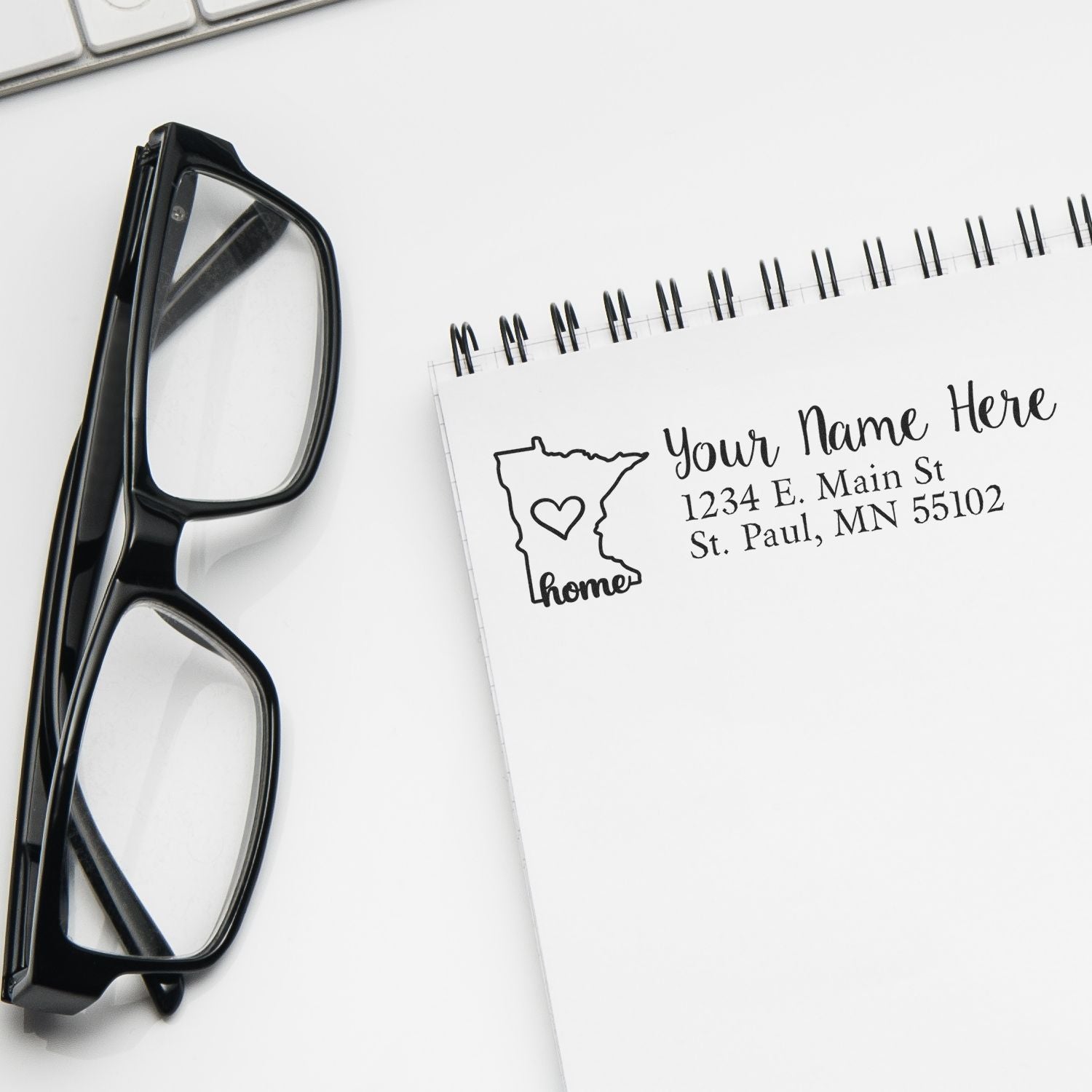 Custom address rubber stamp sample with Minnesota home design on notebook beside eyeglasses