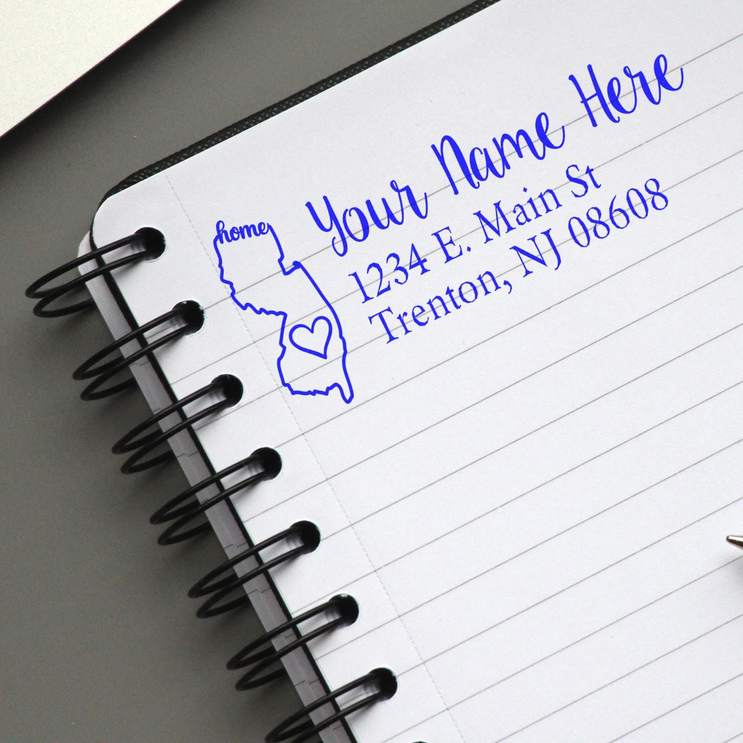 Custom address rubber stamp with name, street address, and New Jersey state outline on notebook paper.