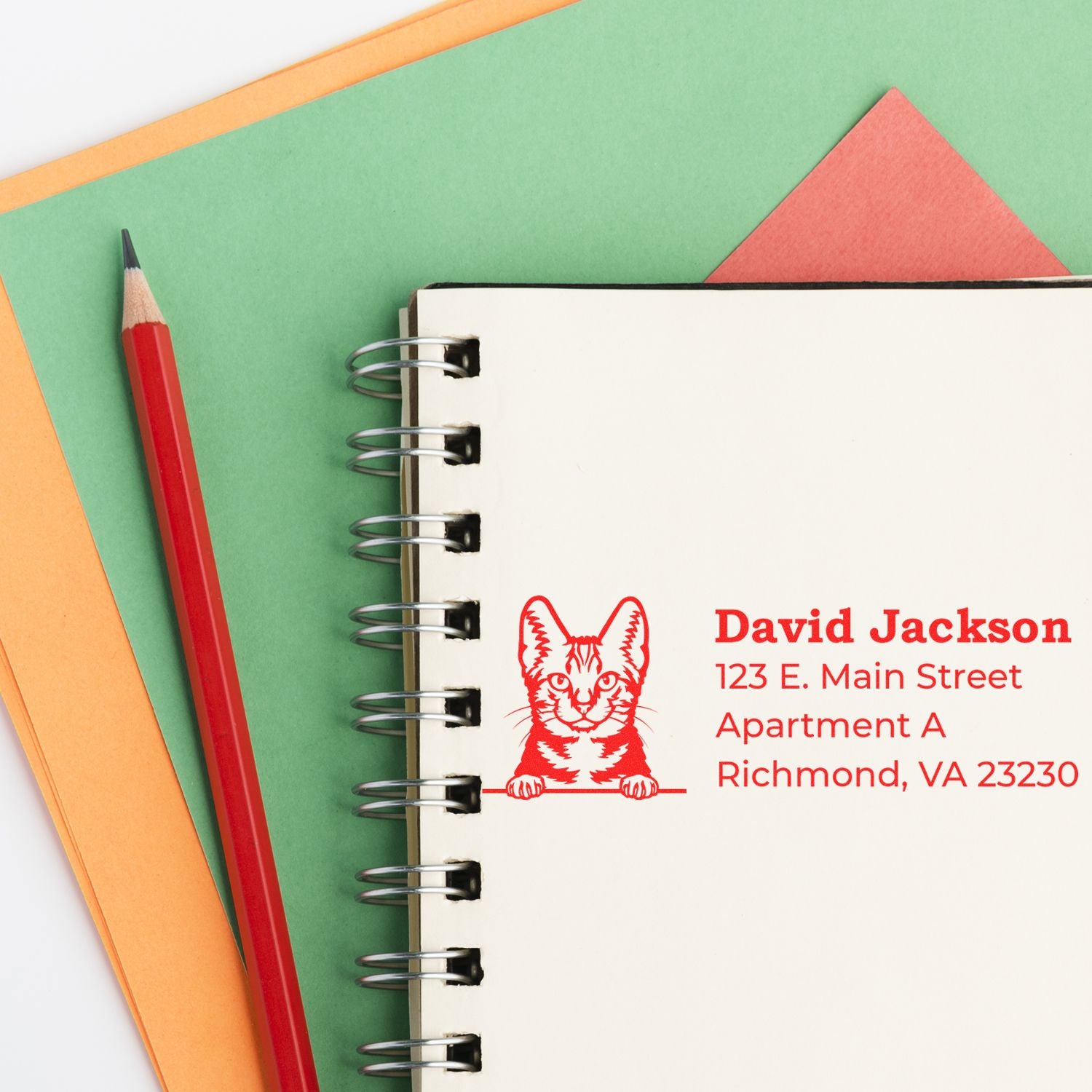 Custom red address rubber stamp with cat logo on a notebook, featuring personalized return address details.