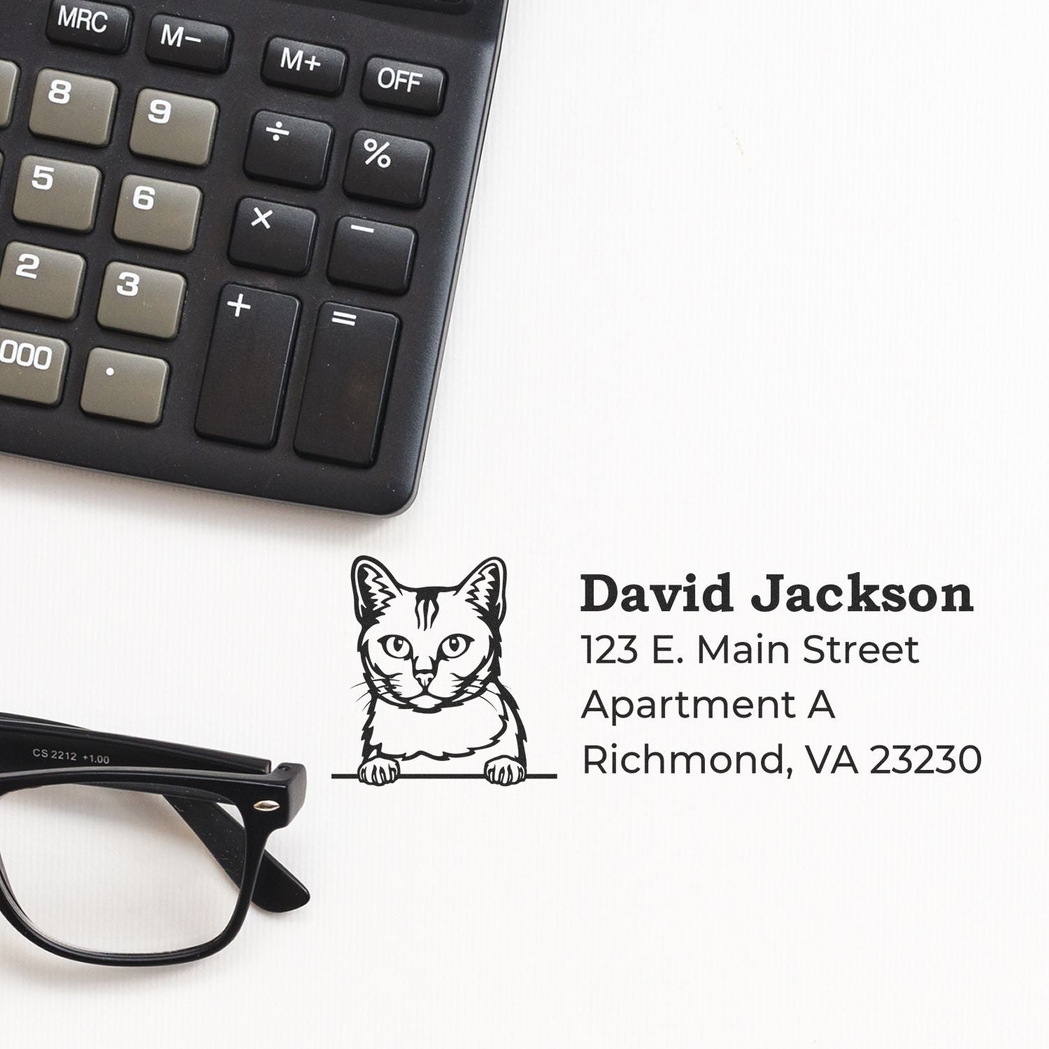 Personalized return address rubber stamp with cat design for David Jackson, Richmond, VA, beside calculator and glasses.