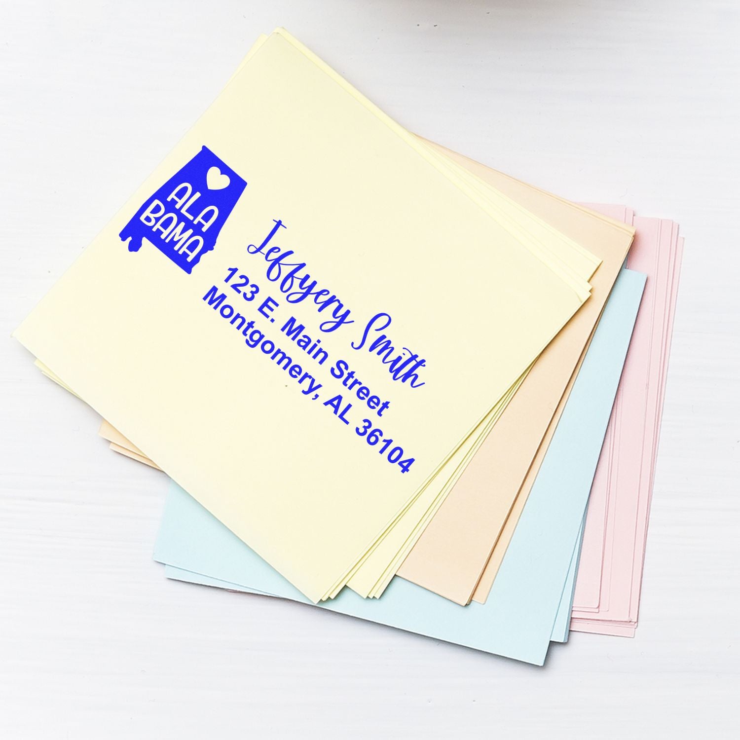 Custom return address rubber stamp on pastel envelopes, showing Jeffery Smith, 123 E. Main Street, Montgomery, AL 36104.