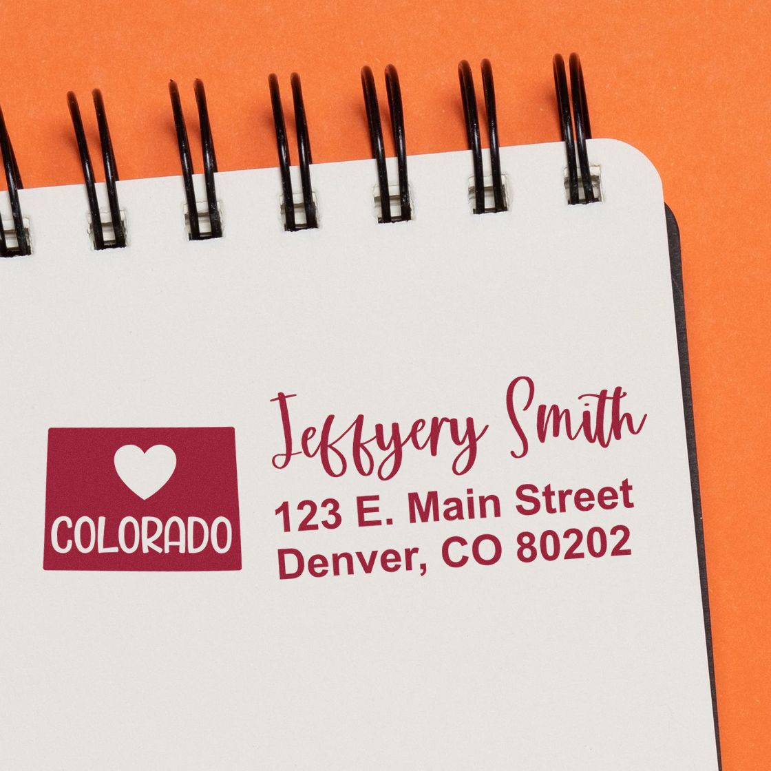 Custom return address rubber stamp with Colorado heart icon, personalized name, and Denver, CO address on notebook.
