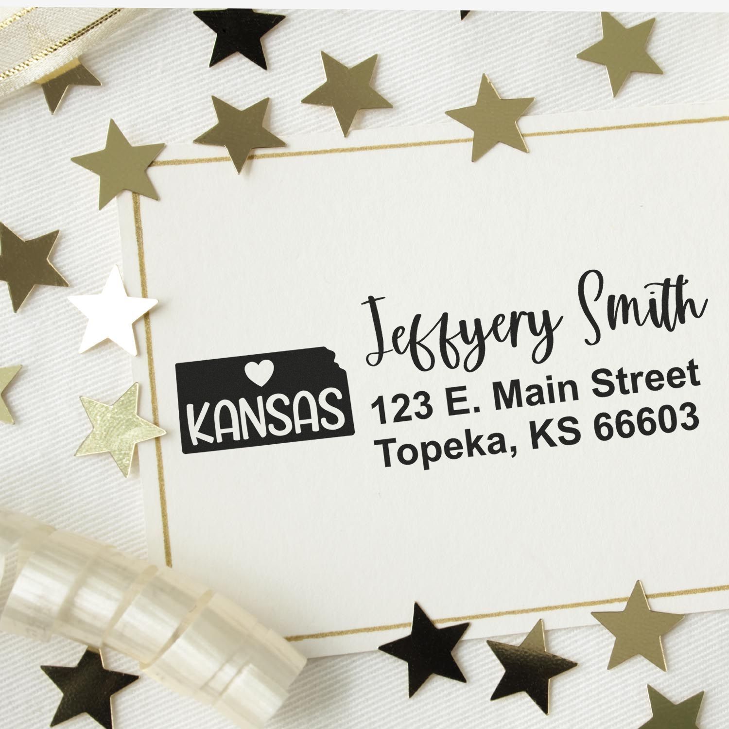 Custom return address rubber stamp for Kansas mailings on a white envelope with gold star confetti.