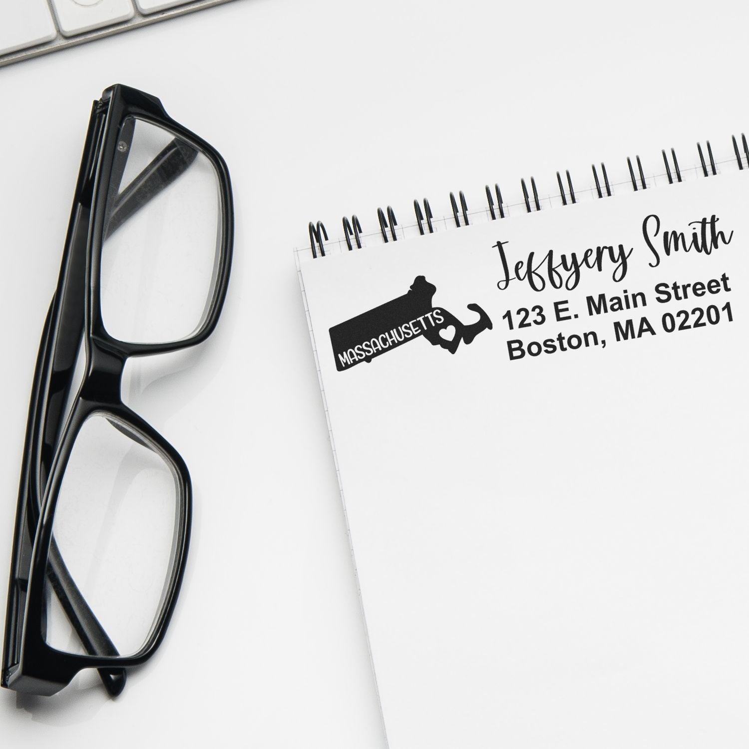 Custom Massachusetts return address rubber stamp for personalized stationery, shown on a notepad beside black eyeglasses.