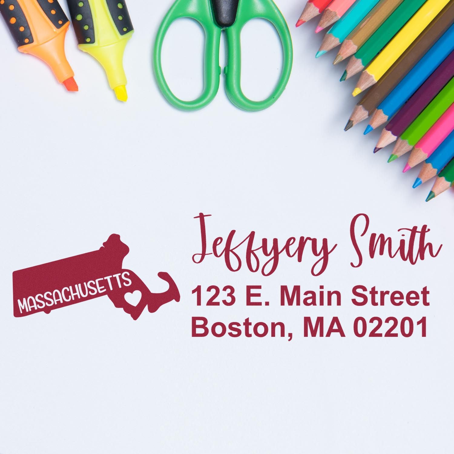 Custom Massachusetts address rubber stamp with name and Boston mailing address, shown with colorful school supplies.