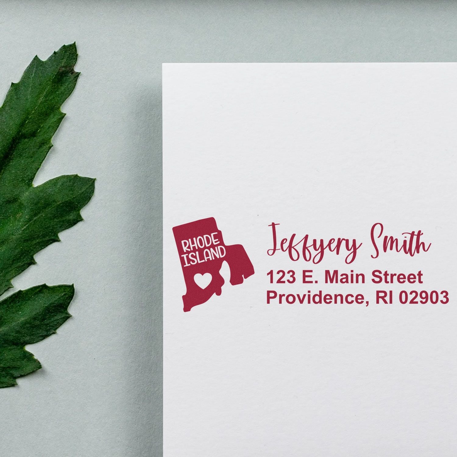 Custom Rhode Island return address rubber stamp with name, address, and state icon printed in red on white envelope.