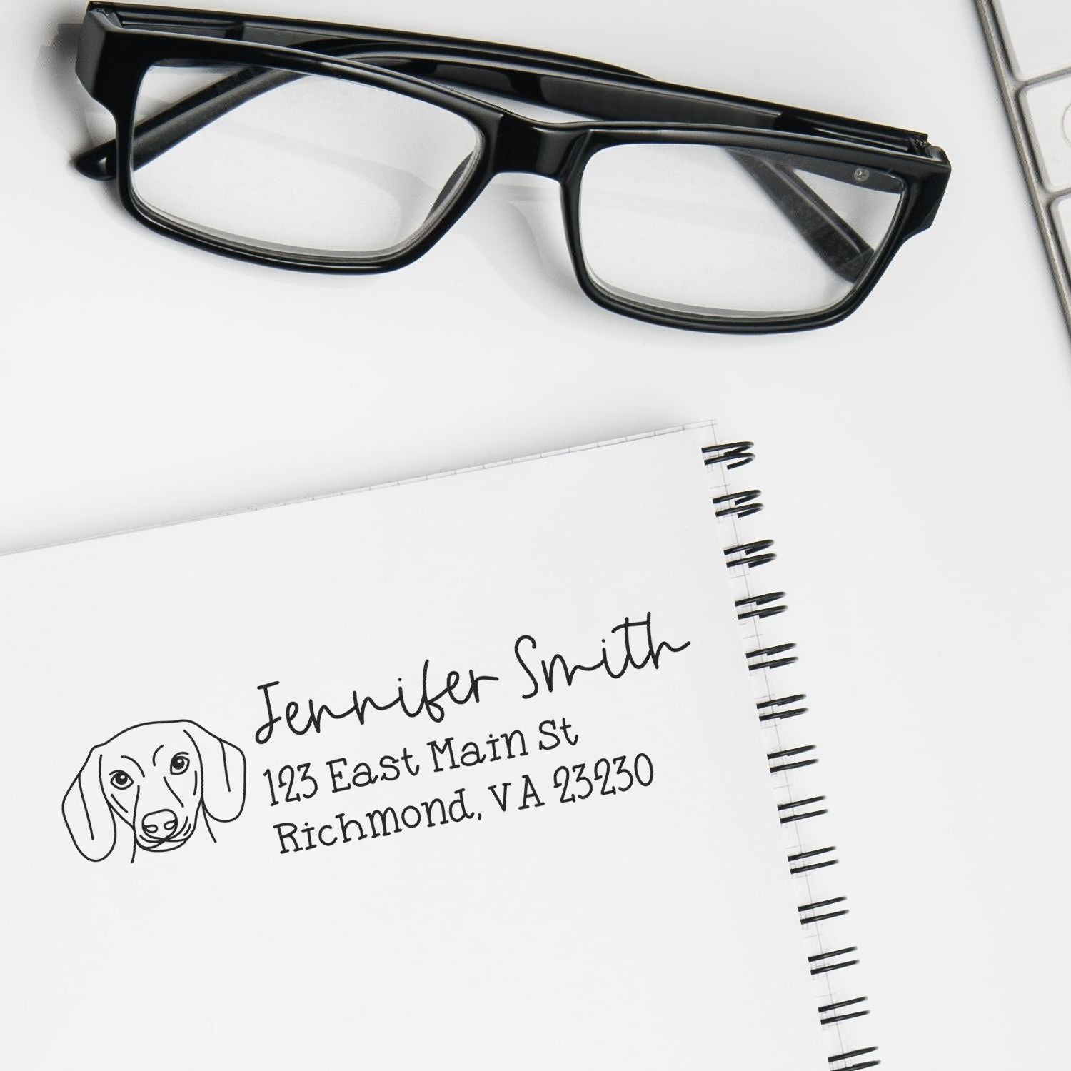 Custom rubber return address stamp with dog icon on notebook page beside eyeglasses, ideal for personalized stationery.