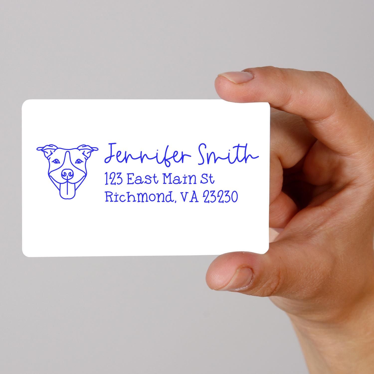 Hand holding custom dog address rubber stamp with personalized name and mailing address in blue ink.