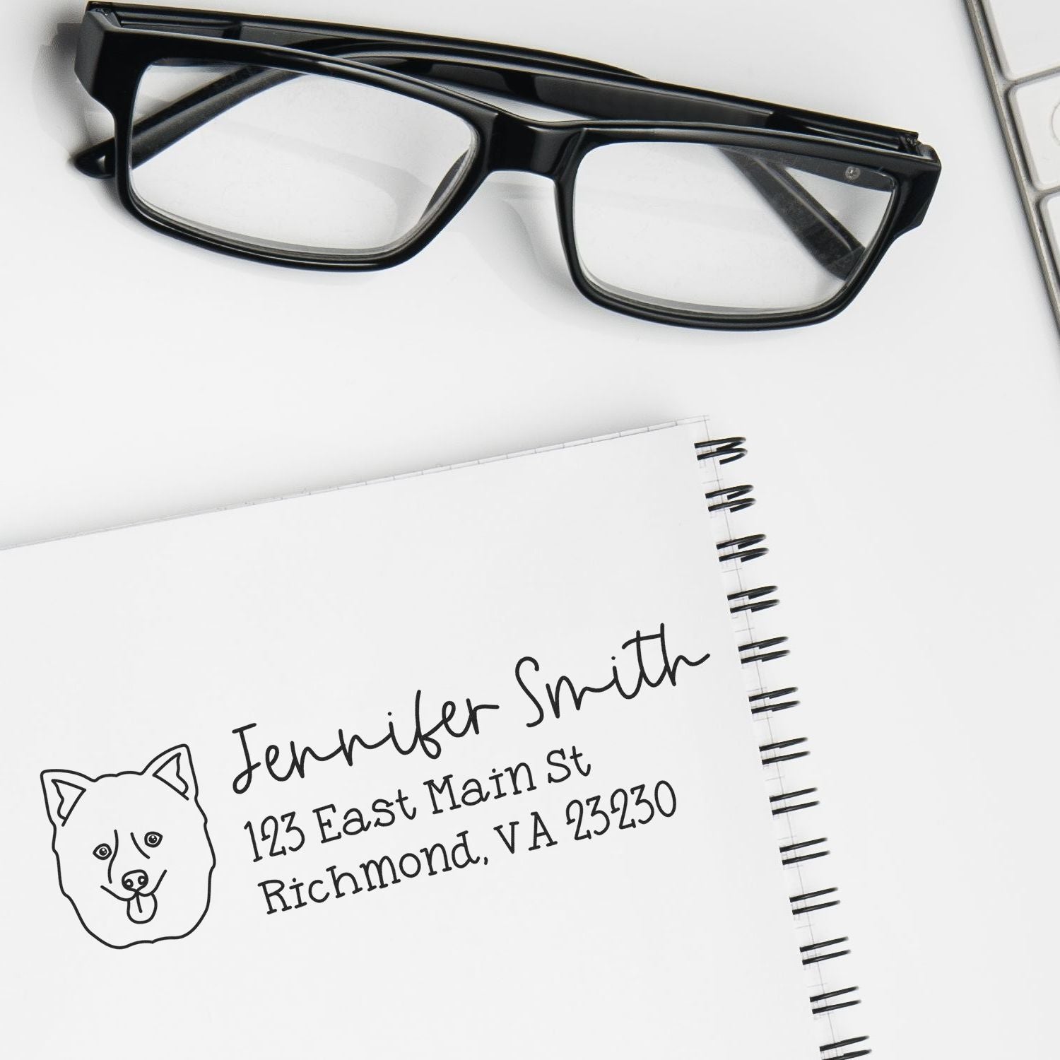 Custom rubber return address stamp with dog logo for personal stationery, shown on a notebook beside eyeglasses.