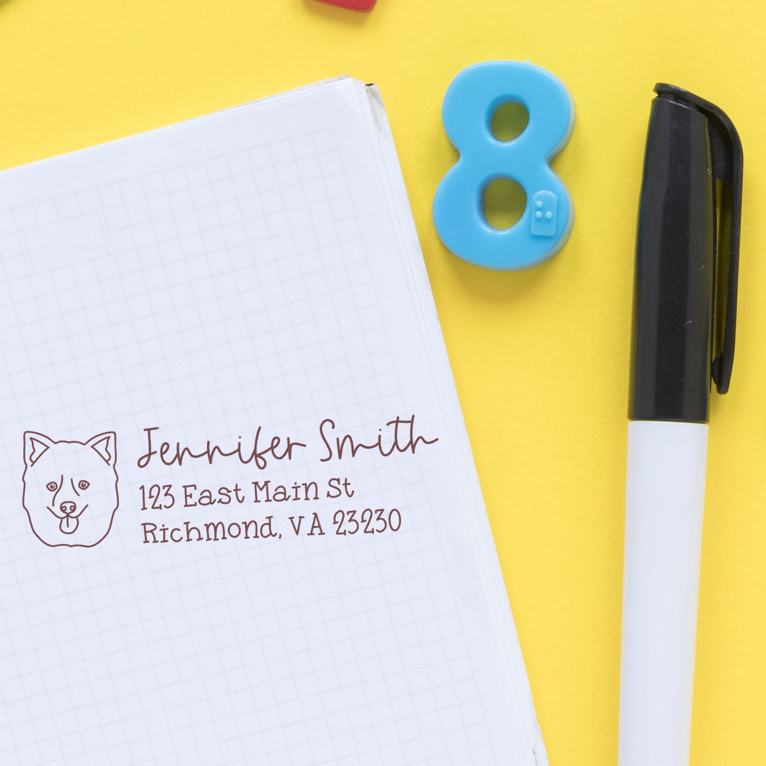 Custom rubber address stamp with dog icon imprinting Jennifer Smiths Richmond, VA return address in a notebook.