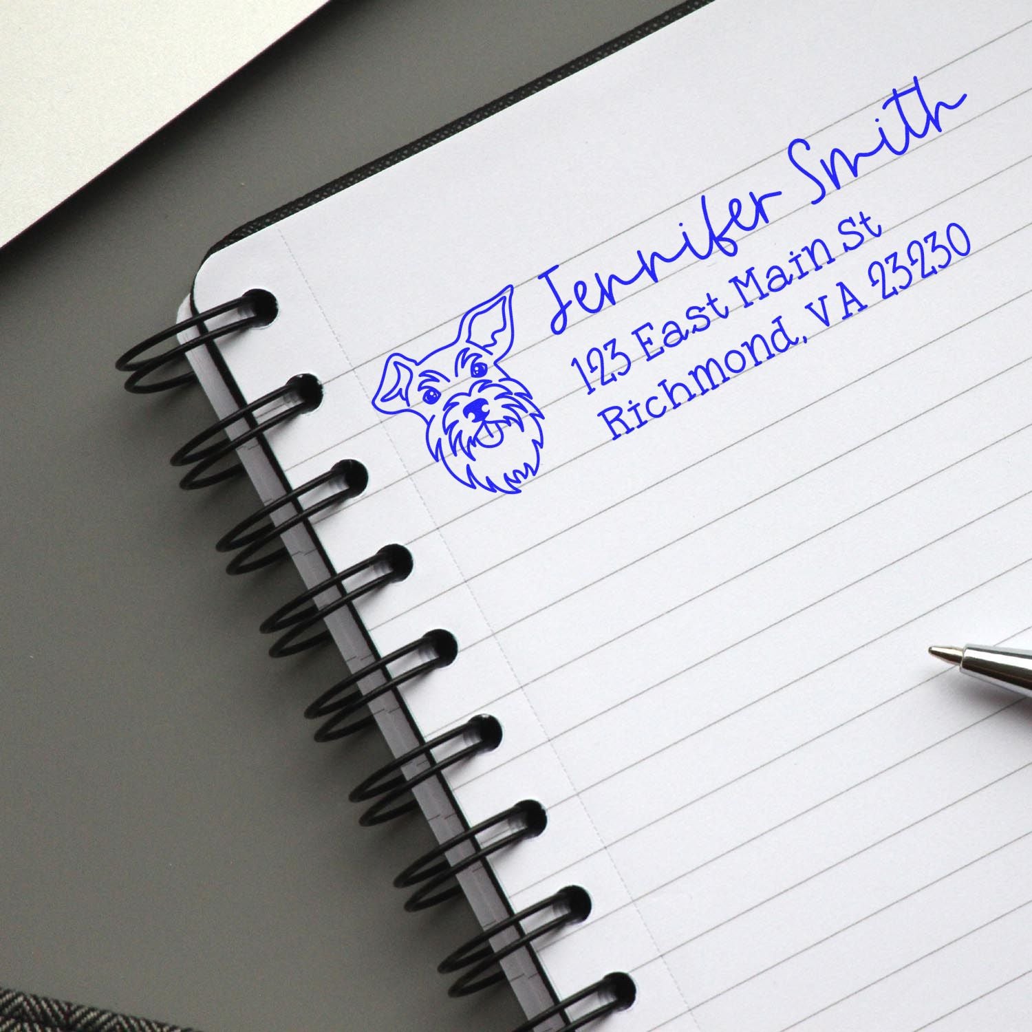 Custom rubber address stamp with dog logo, Jennifer Smith name, and Richmond VA address stamped in blue ink on notebook paper.