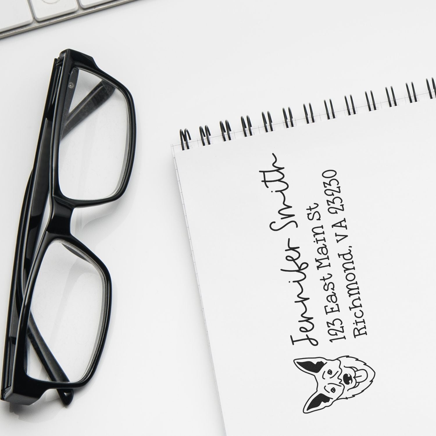 Personalized return address rubber stamp with dog logo beside eyeglasses and notebook.