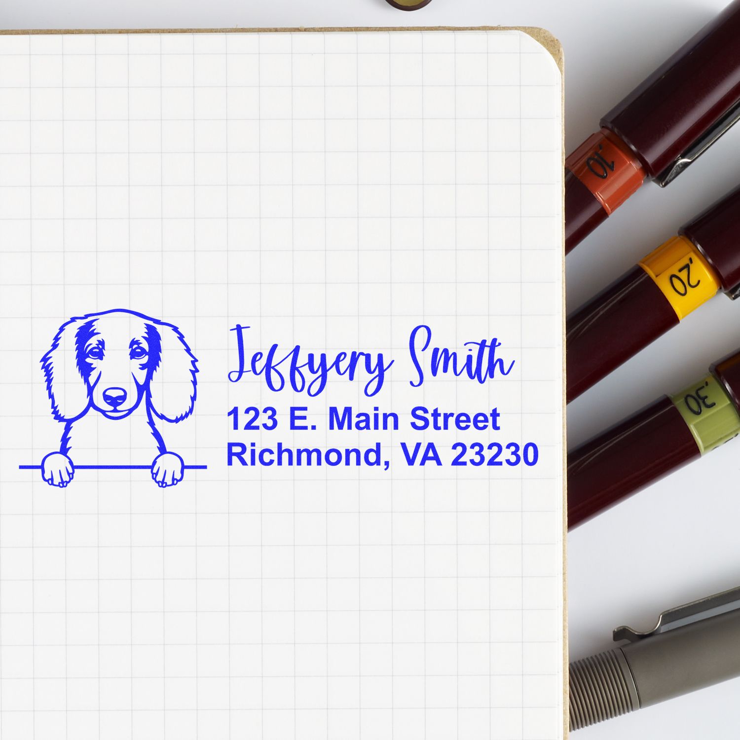 Personalized pet return address rubber stamp with dog illustration and name on notebook, beside ink stamp pens.