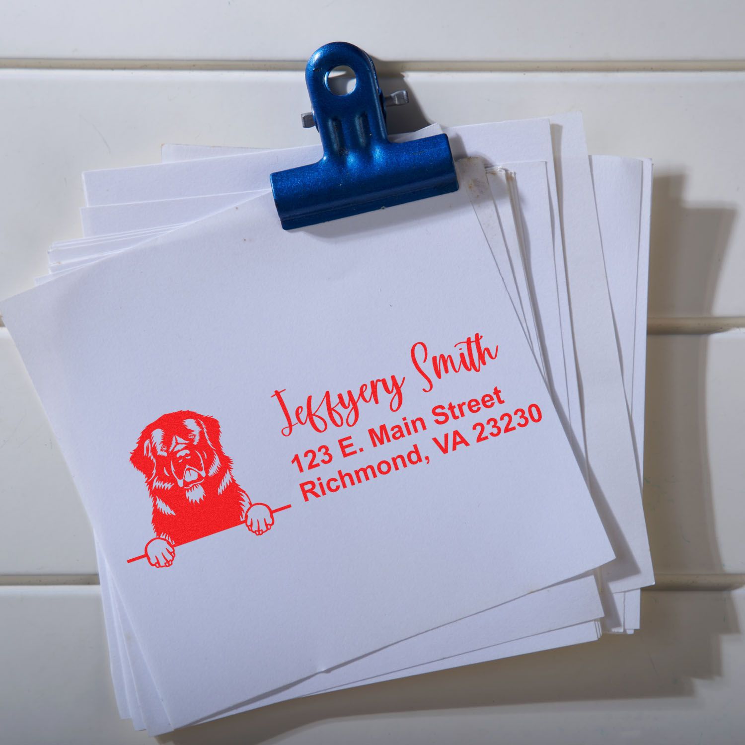 Custom rubber return address stamp with dog logo and personalized name and address on stacked envelopes.