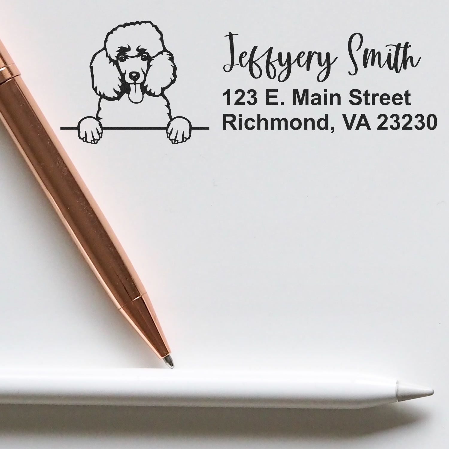 Custom poodle return address rubber stamp with name and Richmond, VA address, shown stamped on paper with pen.