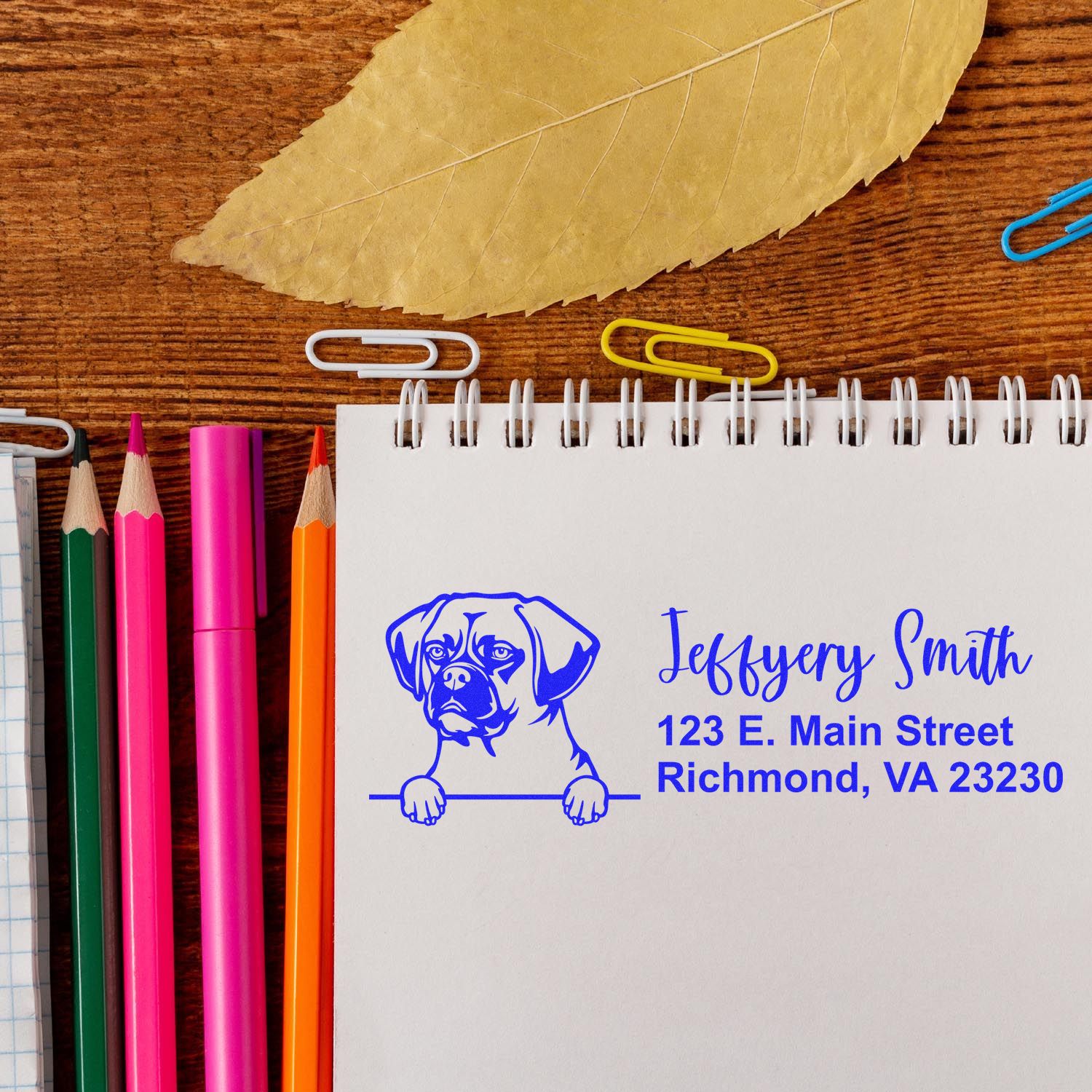 Custom rubber stamp with dog logo, name, and address on a notebook, showcasing personalized business stationery.