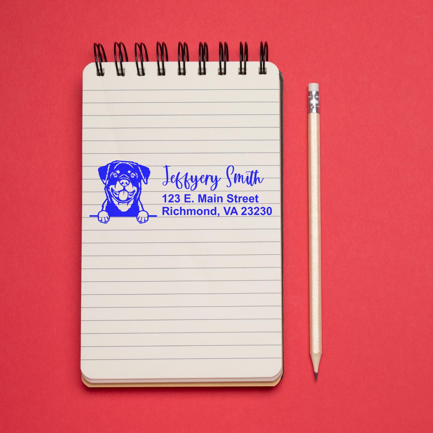 Custom return address rubber stamp with dog logo on a lined notebook beside a pencil.