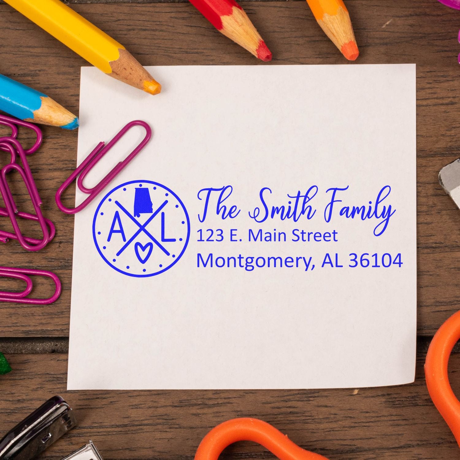 Custom return address rubber stamp with family name and address, shown on paper with colorful school supplies.