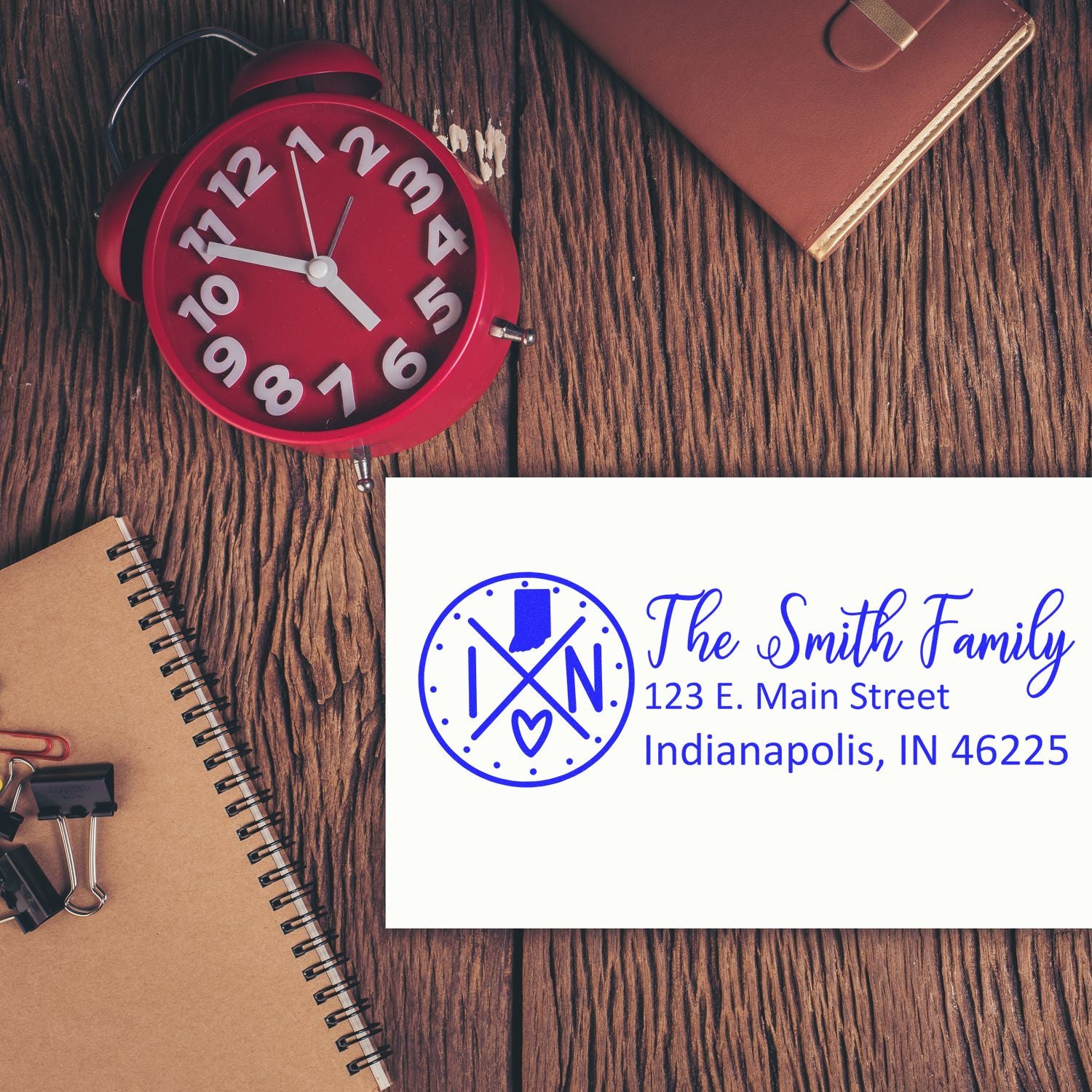 Custom rubber address stamp sample with family monogram, name, and Indianapolis return address on a desk flat lay.