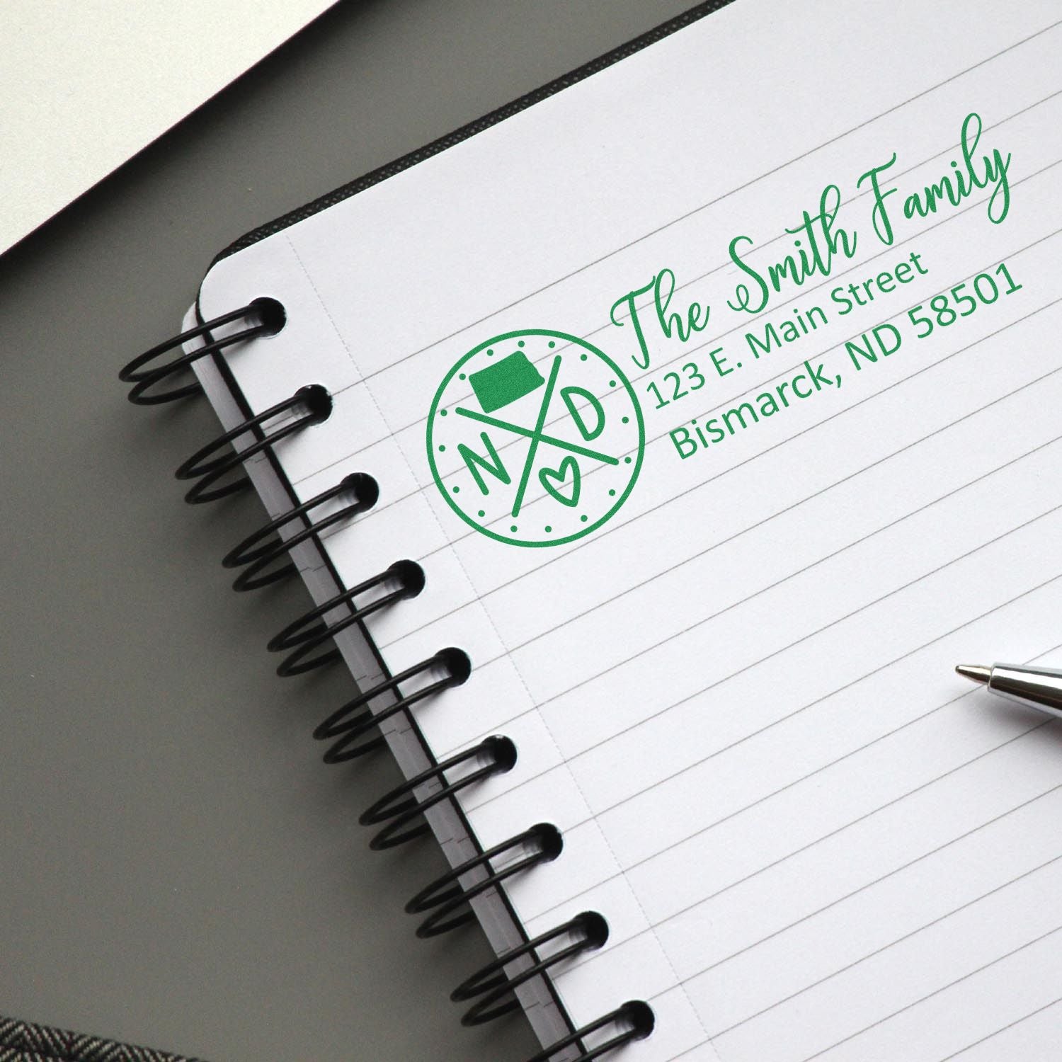 Personalized family address rubber stamp with monogram, shown in green on a notebook page for custom mail branding.