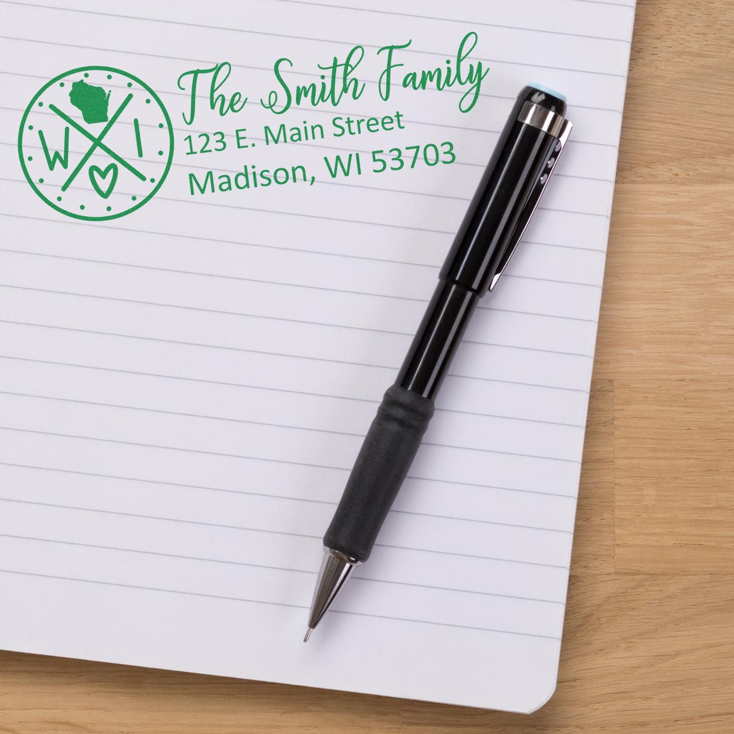 Personalized family return address rubber stamp with Wisconsin design shown on notebook paper beside a pen.
