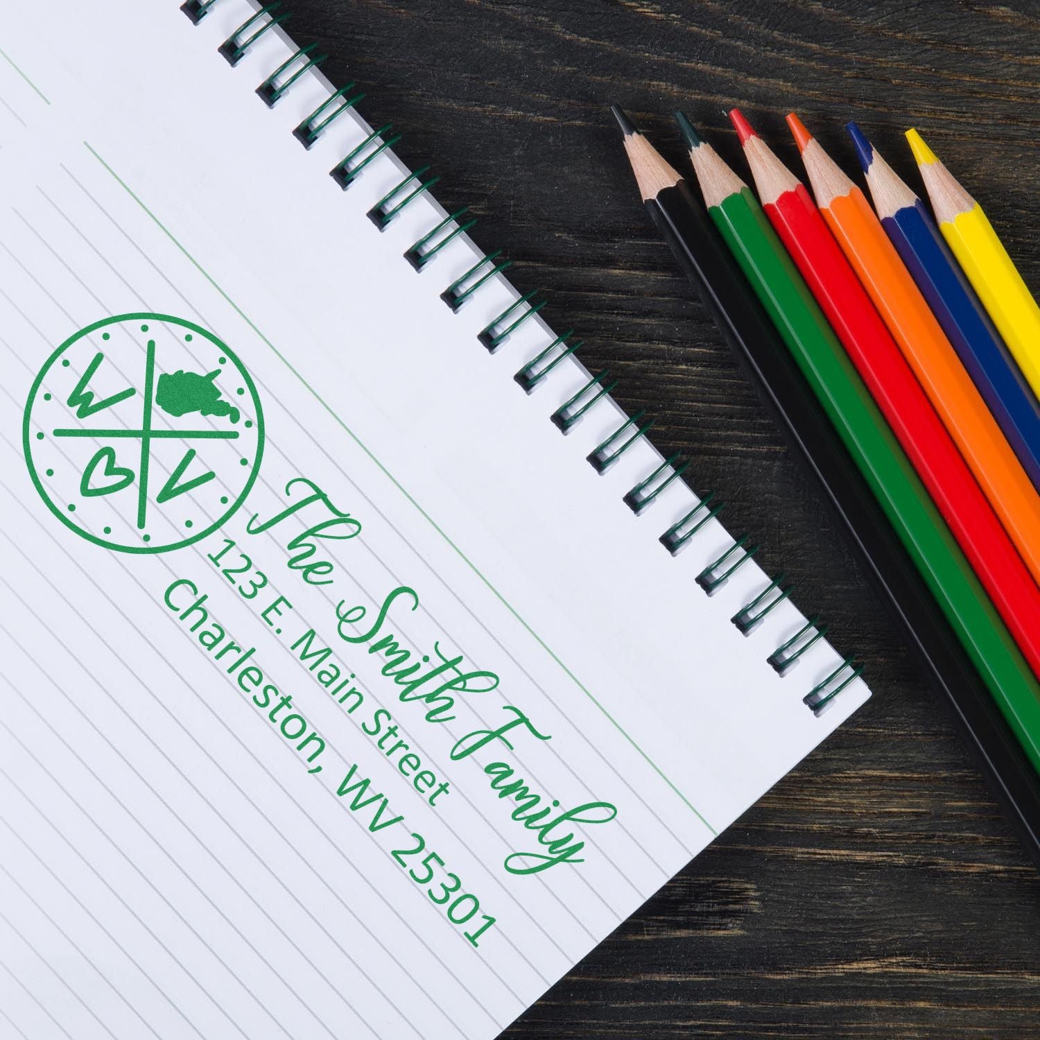 Custom family return address rubber stamp on notebook paper beside colored pencils