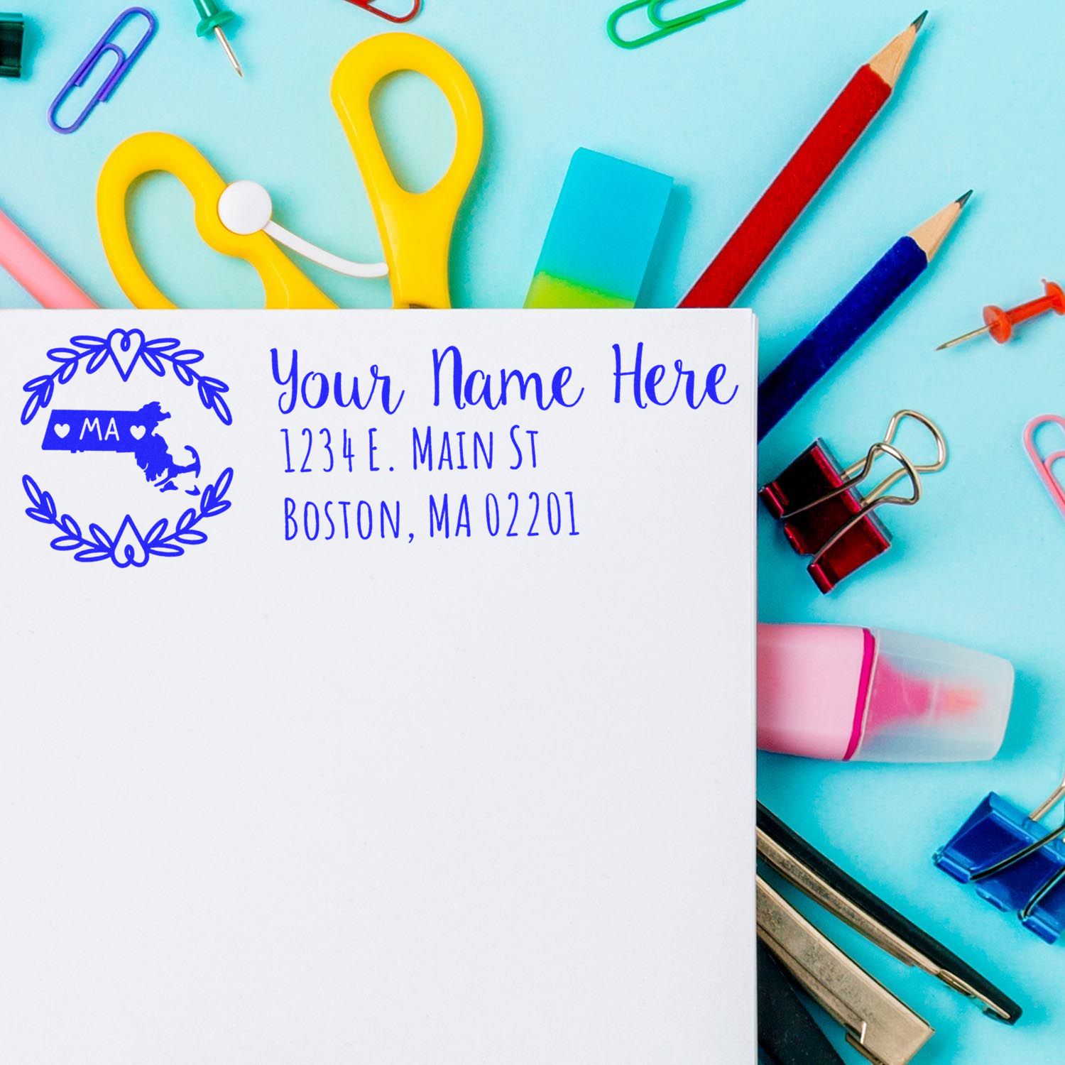 Custom return address rubber stamp with name and Boston, MA address on envelope, shown with colorful stationery supplies.