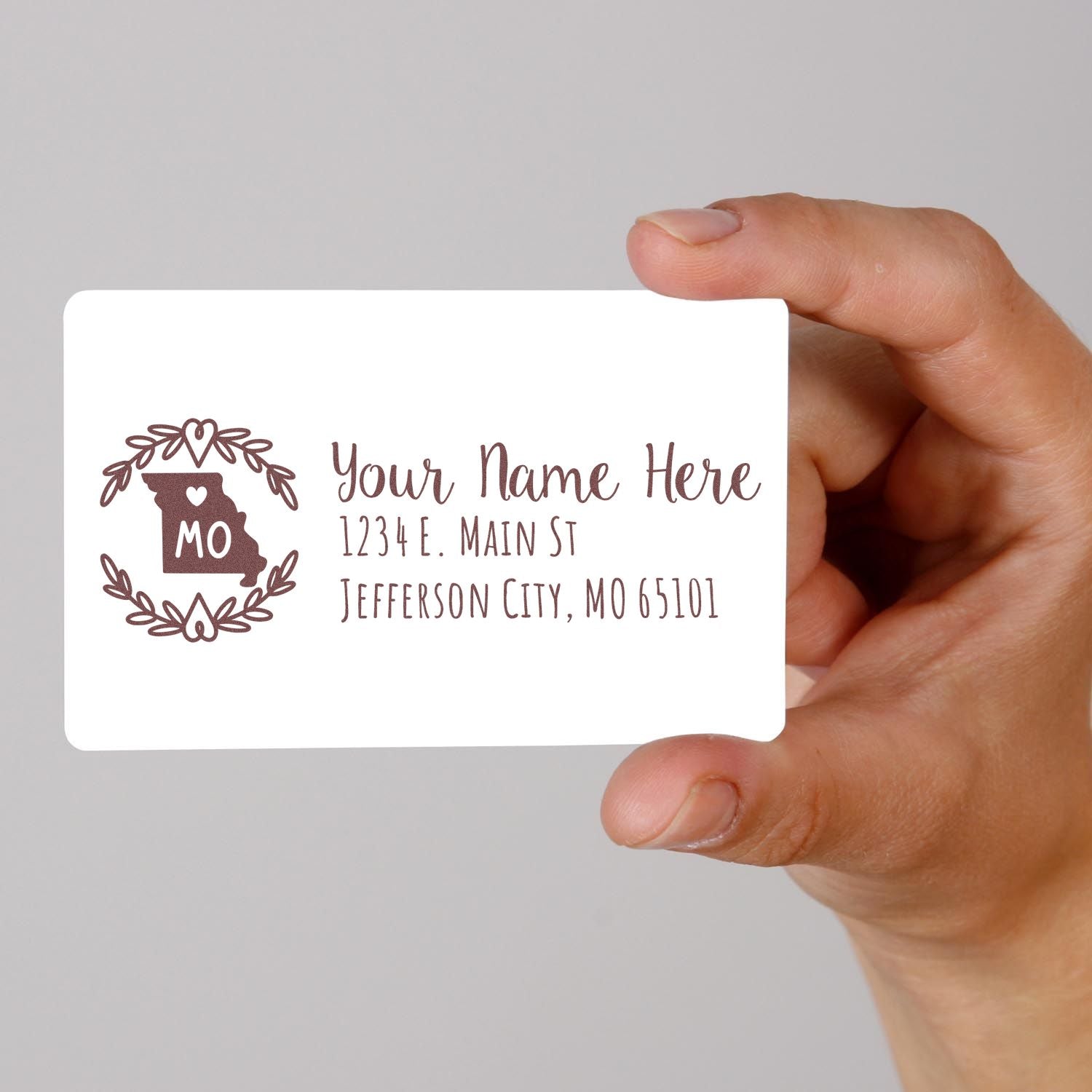 Hand holding custom return address rubber stamp with Missouri monogram, name, and address for personalized mailing.