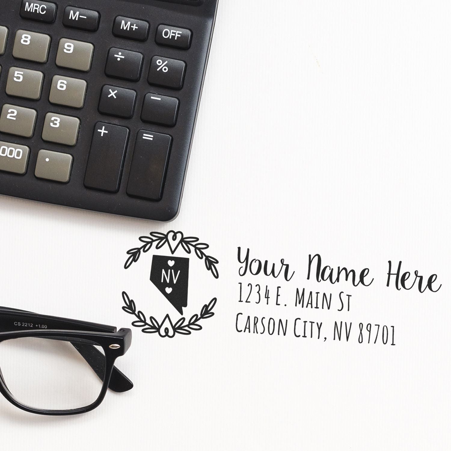 Custom address rubber stamp proof with Nevada monogram design and personalized mailing details, beside calculator and glasses.
