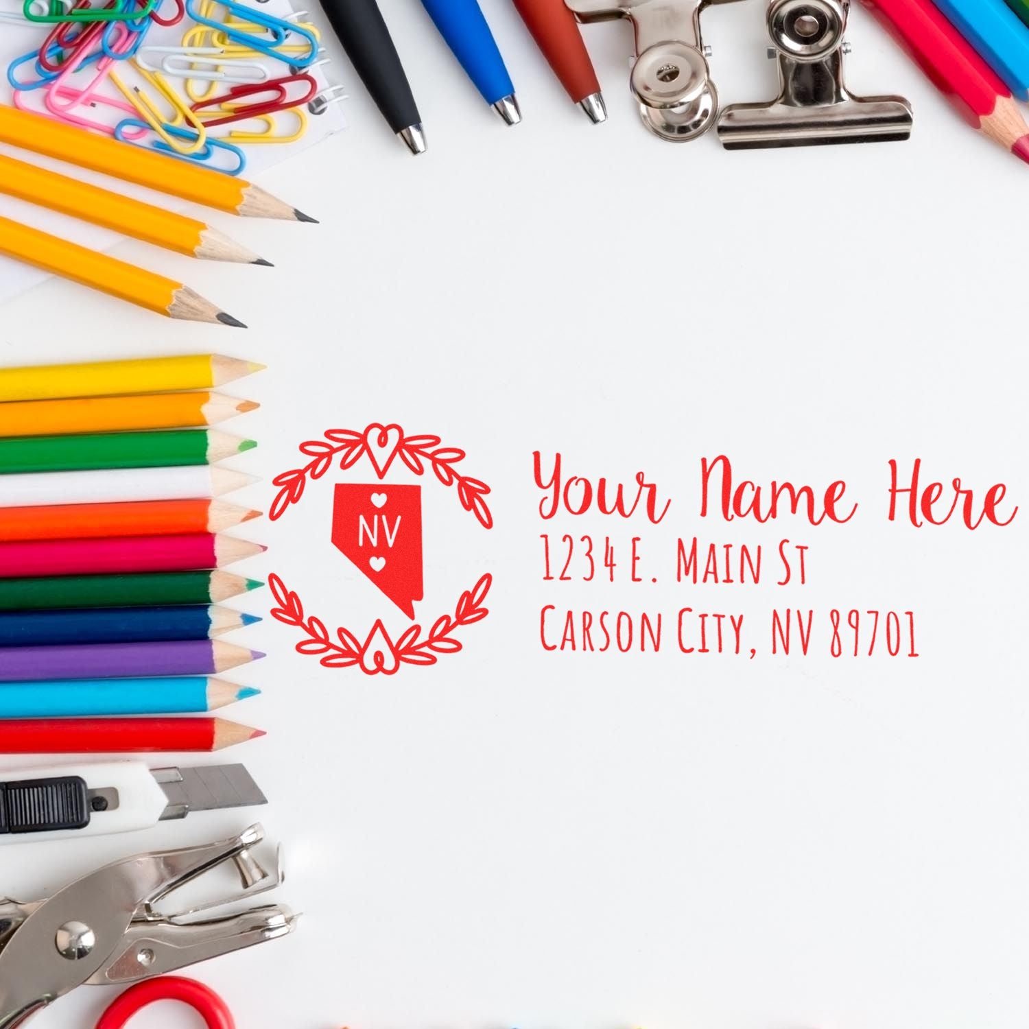 Custom rubber stamp sample with personalized Nevada address design, framed by colorful pencils and office supplies.