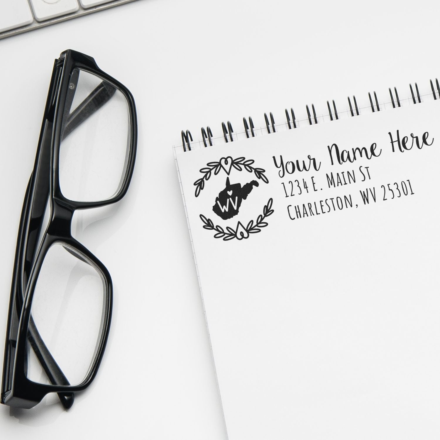 Custom return address rubber stamp with West Virginia state design, stamped on a notebook beside black eyeglasses.