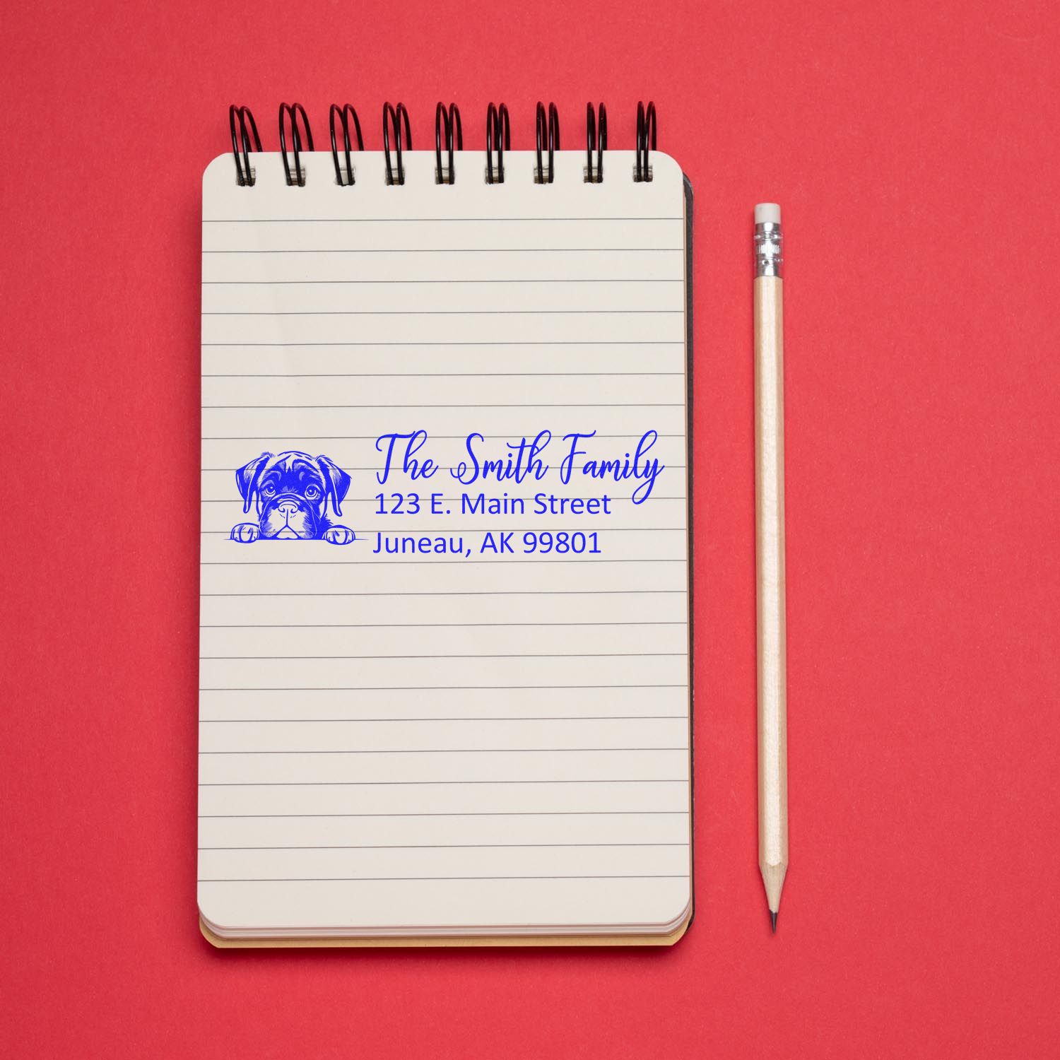 Custom dog address rubber stamp with family name and return address, shown on a notebook beside a pencil.