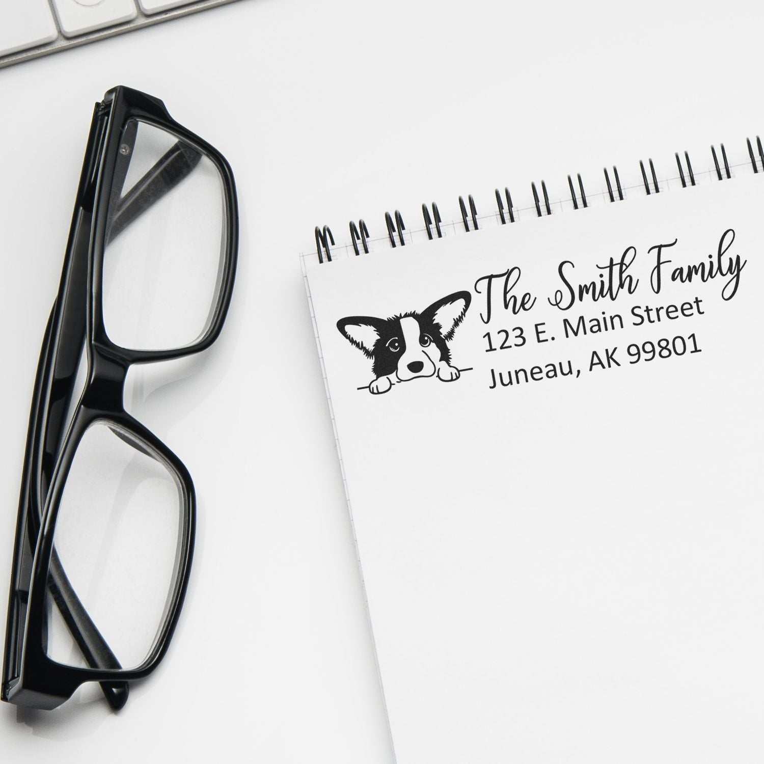 Personalized rubber address stamp with corgi design for family mailings, shown on a notebook beside eyeglasses.
