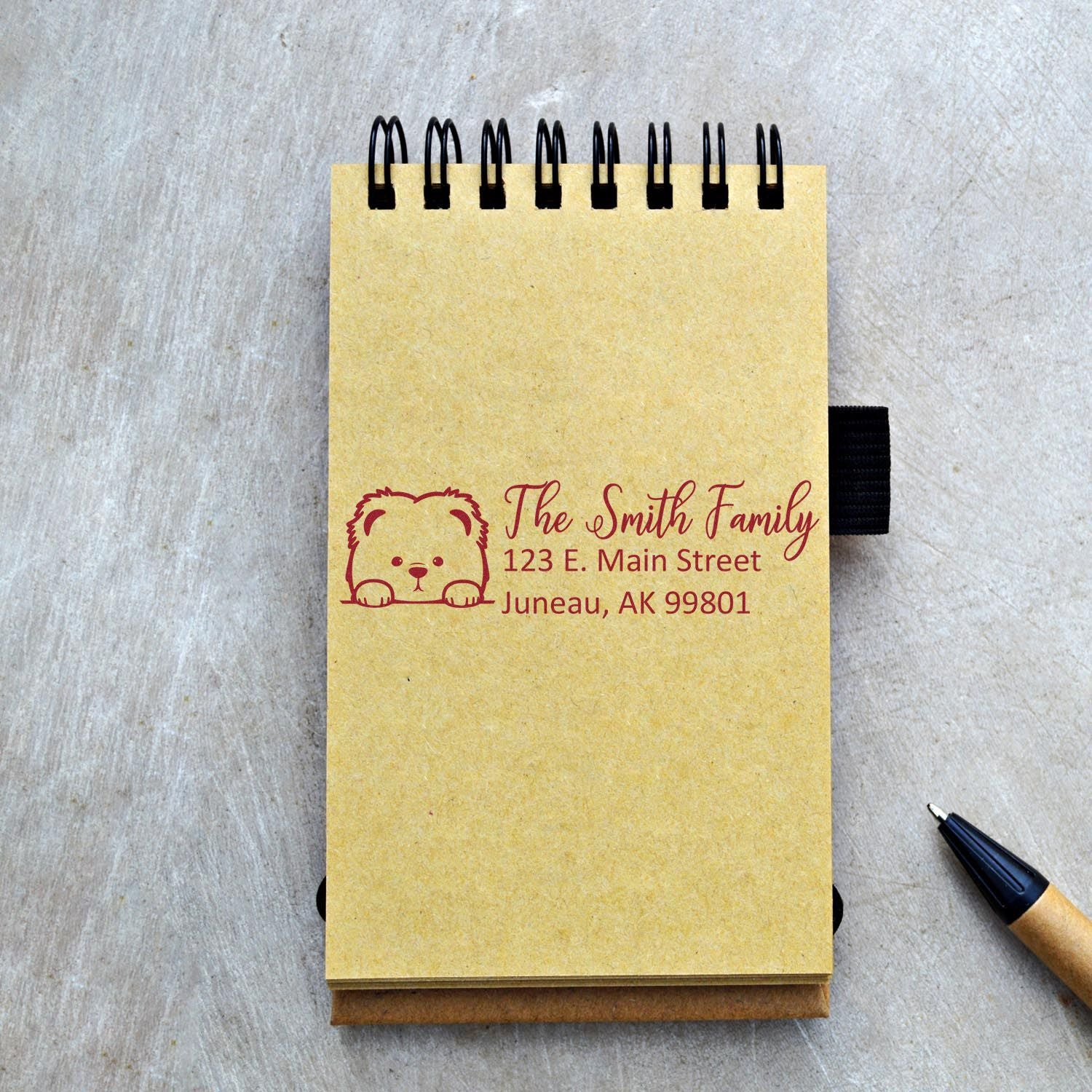 Personalized rubber return address stamp with bear logo and family name on a notepad.