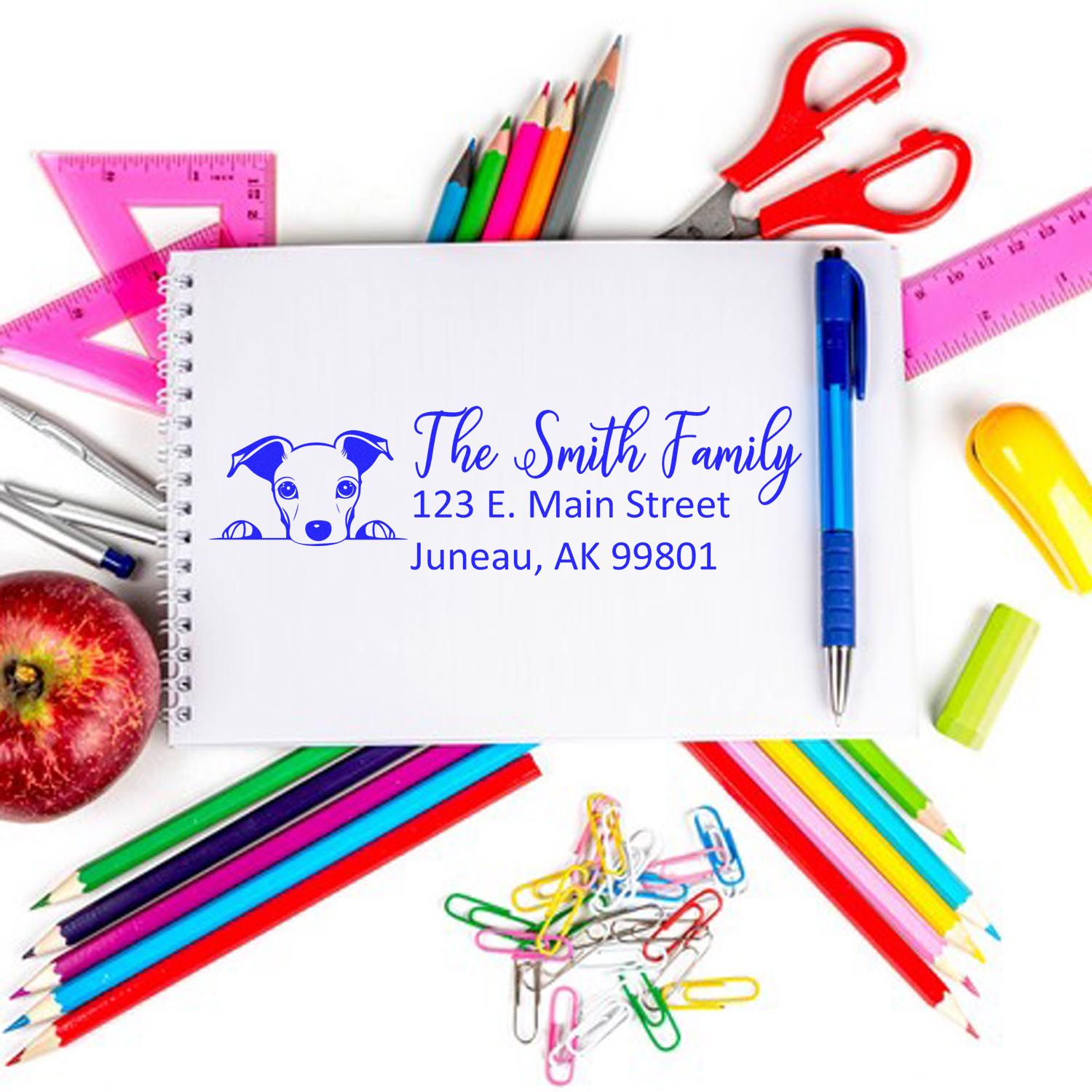 Personalized rubber return address stamp with dog icon for The Smith Family, shown on notebook with school supplies.