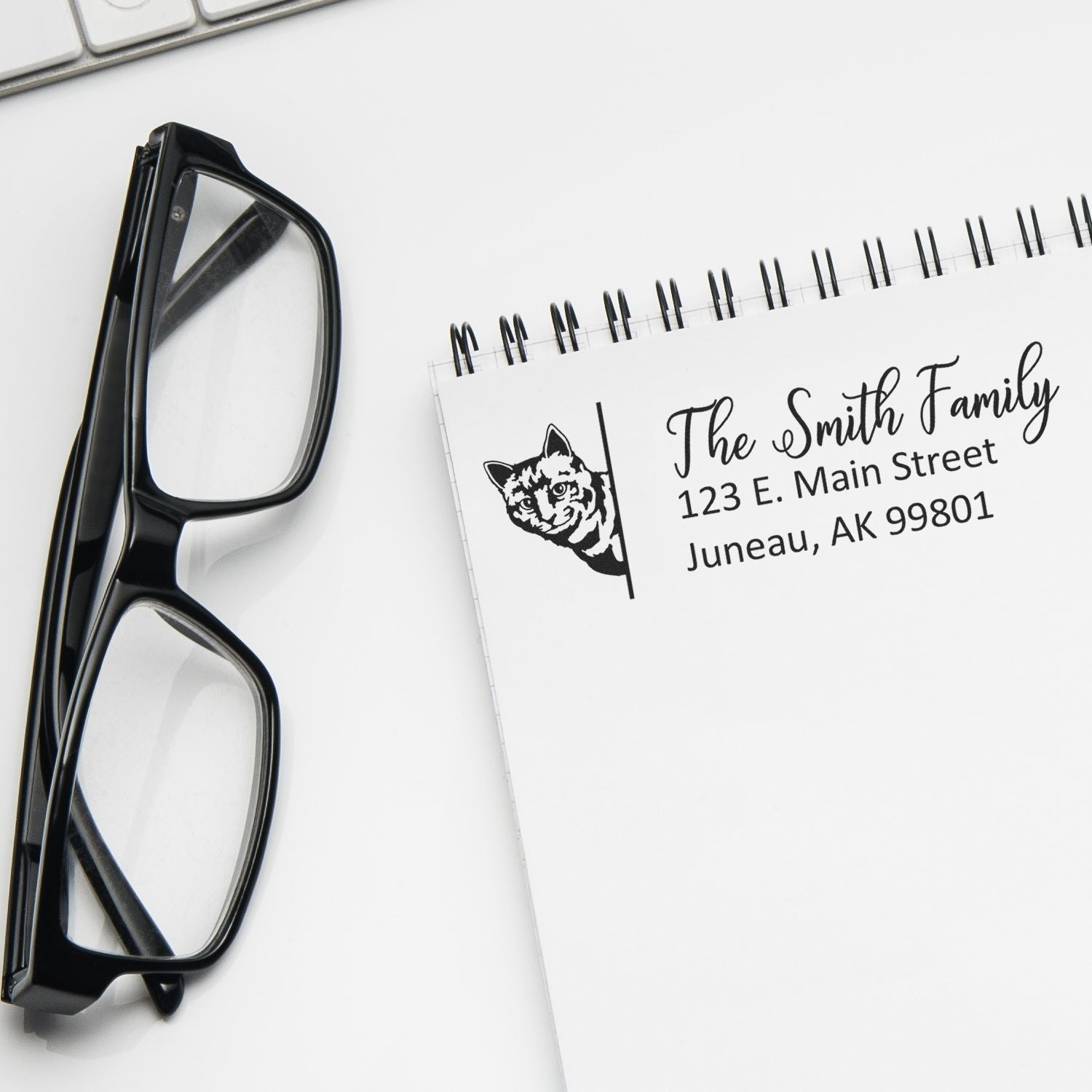Custom rubber address stamp with cat design for The Smith Family return mailing label on a notepad beside eyeglasses