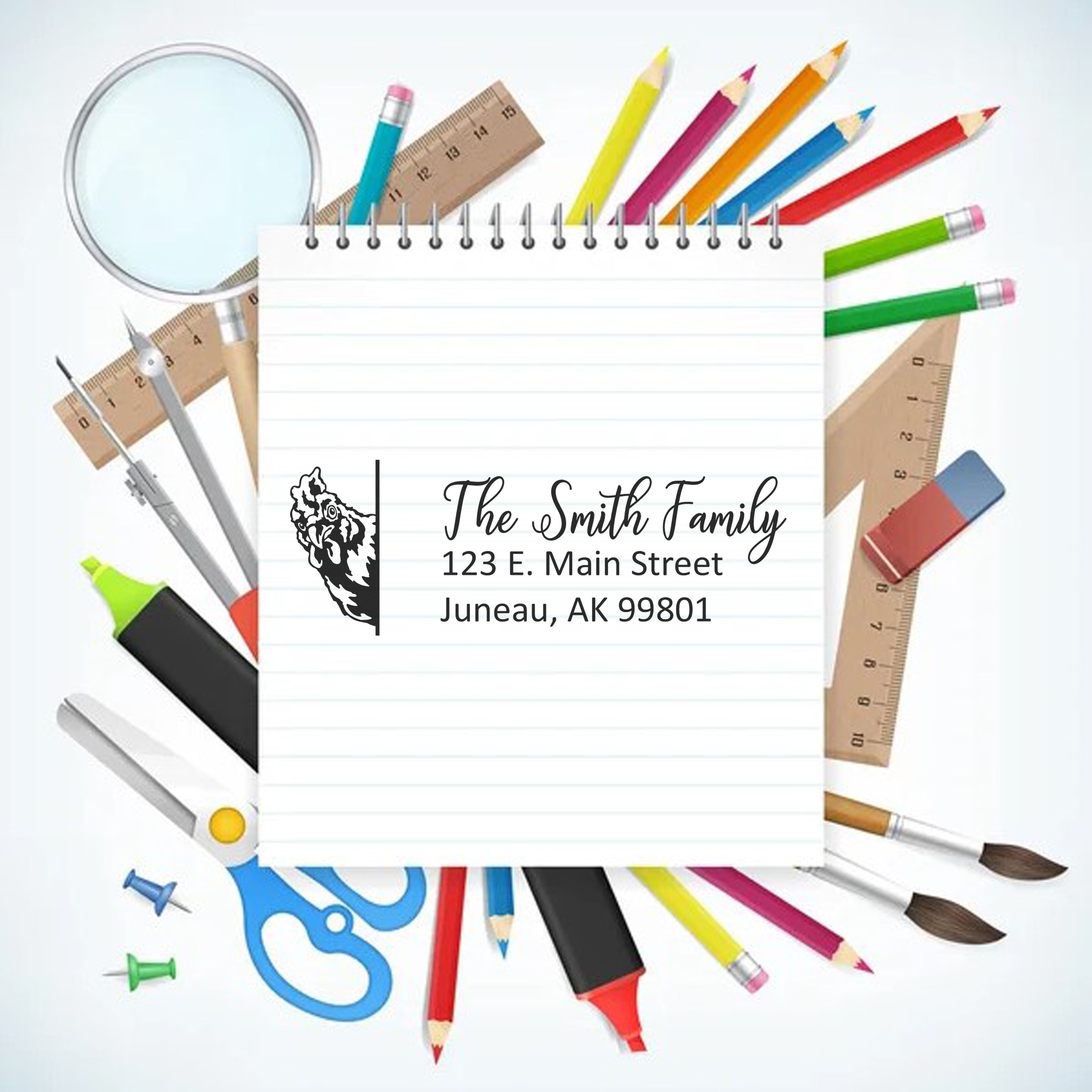 Custom rubber stamp with family name and address on notebook, surrounded by school supplies and pencils.